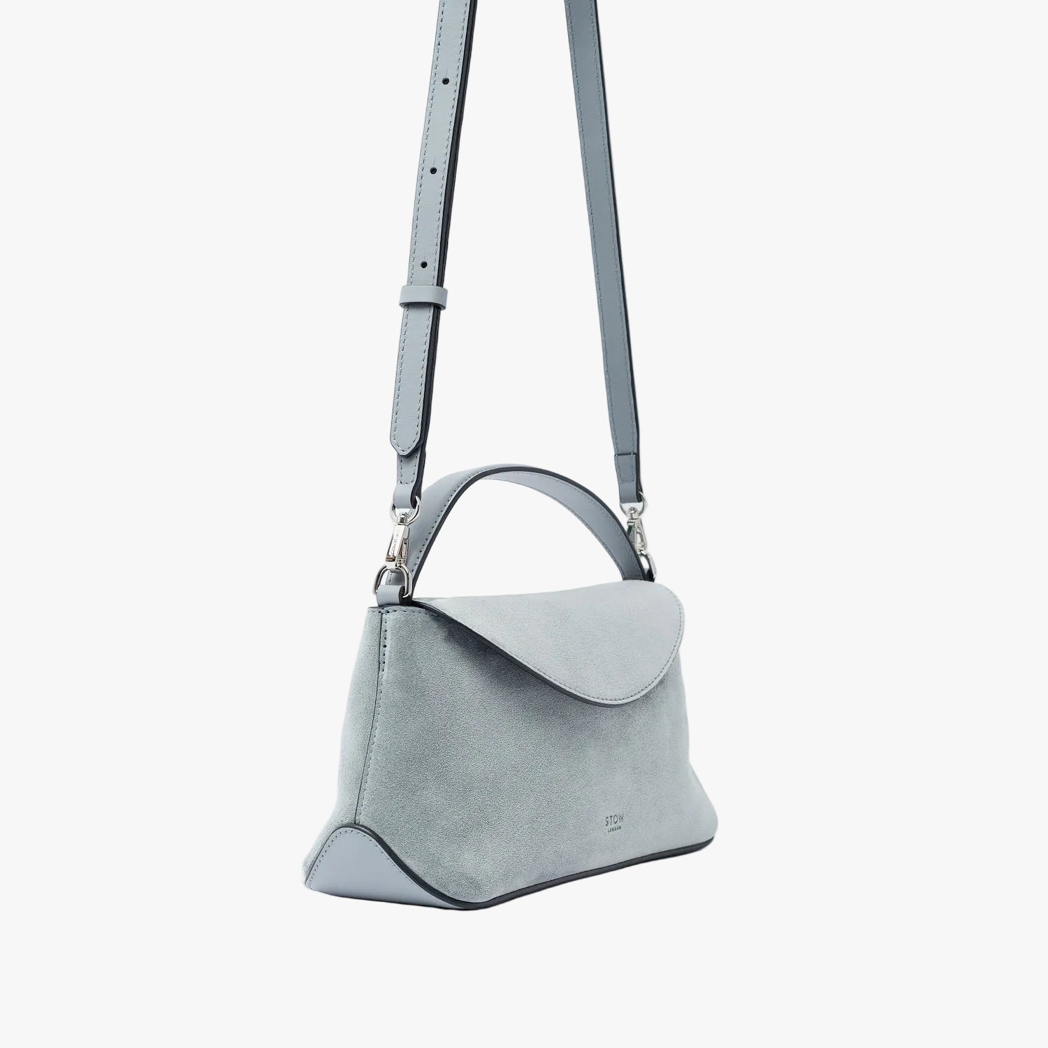Off-axis view of STOW London's Mini East West in Misty Blue suede leather and detachable crossbody strap featuring silver stainless steel hardware on a light grey background