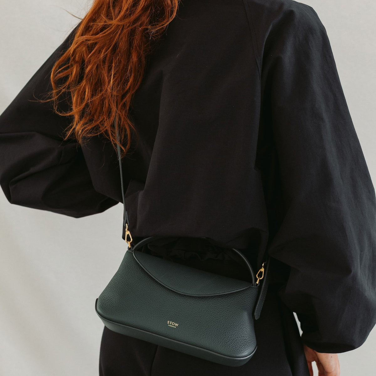 Model in a full black outfit wearing STOW London's Mini East West in New Forest pebbled leather crossbody featuring gold-coated stainless steel hardware