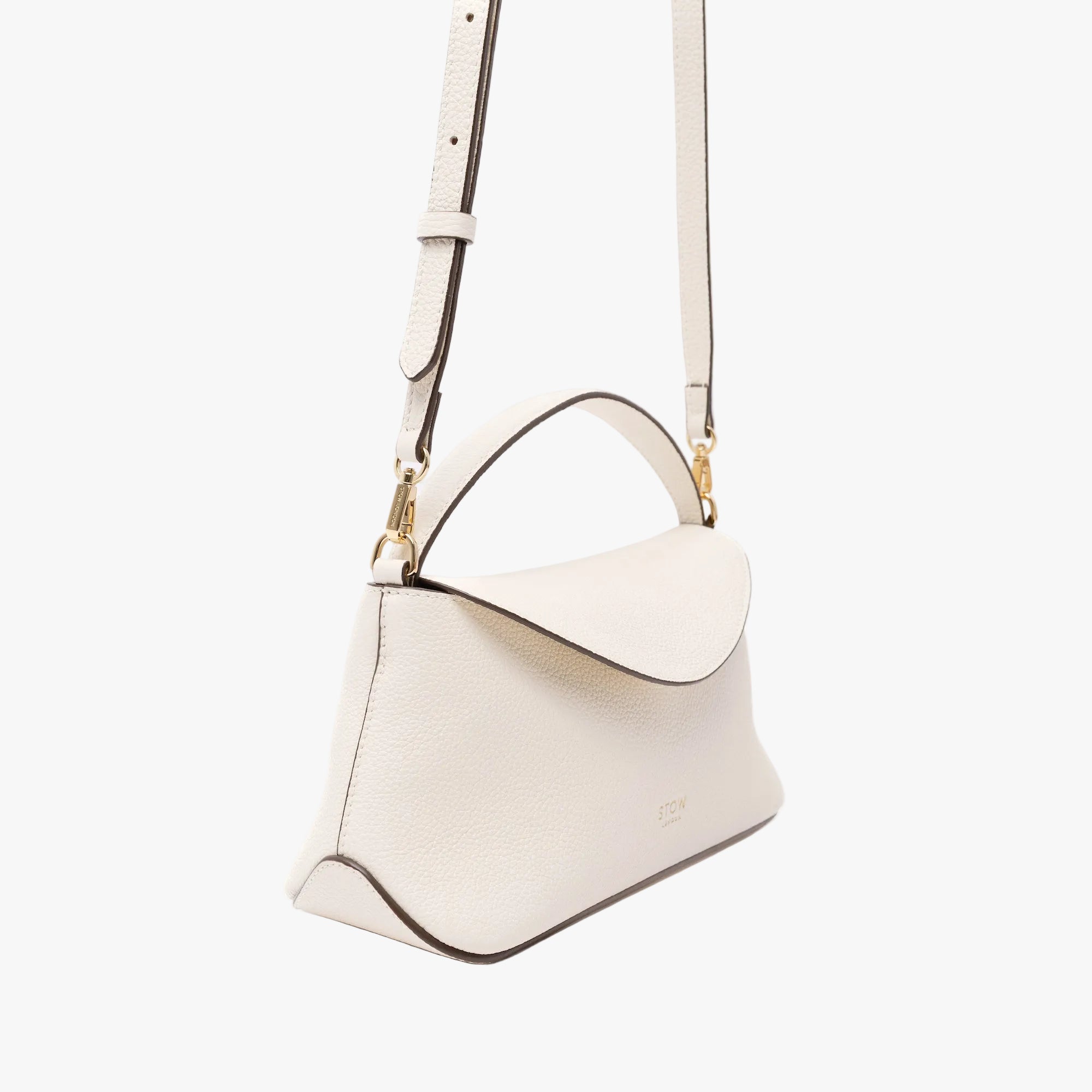 Off-axis view of STOW London's Mini East West in Spring Moon pebbled leather featuring the crossbody strap attached with gold-coated stainless steel hardware on a light grey background