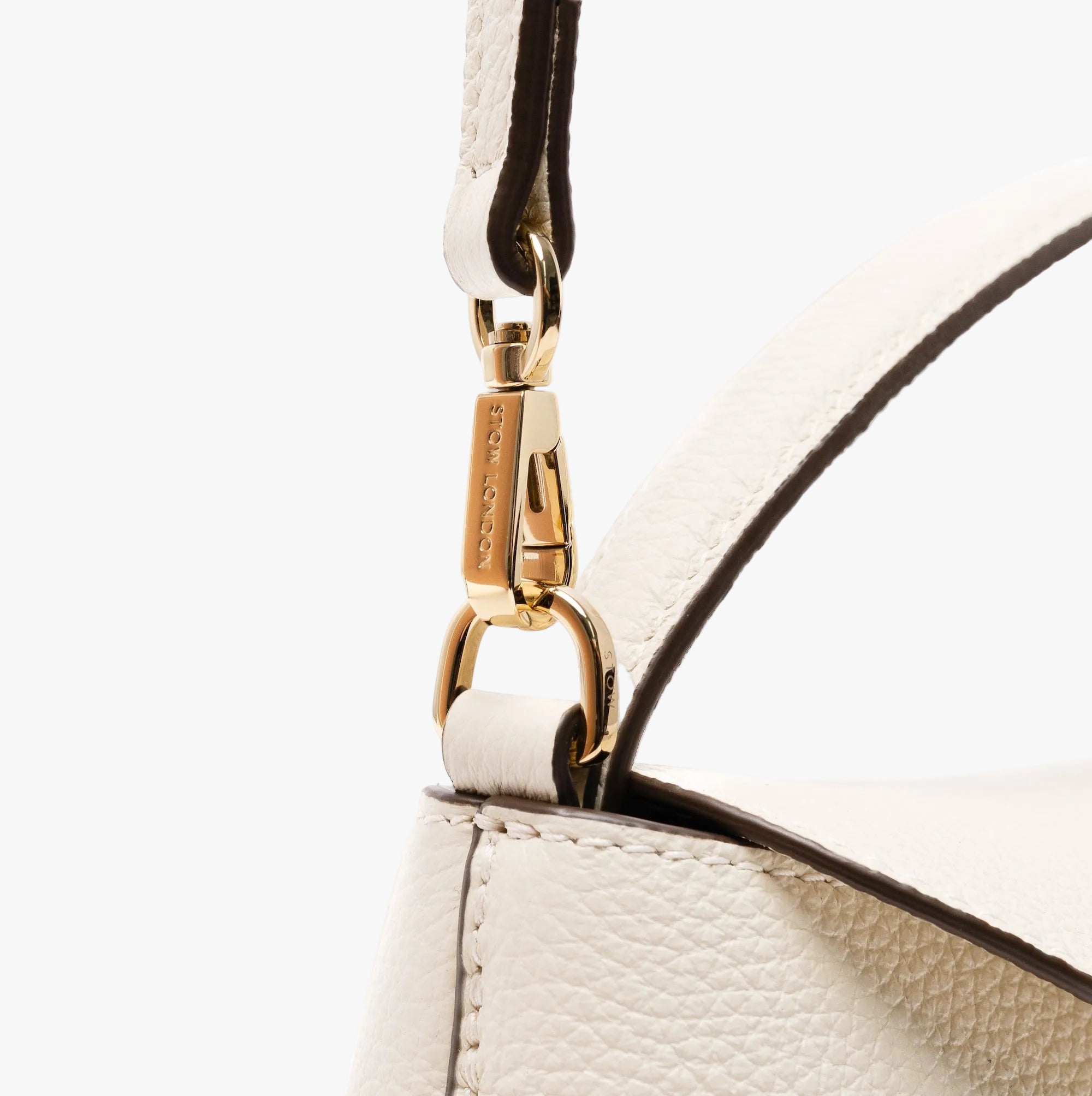 Close up of the detachable crossbody strap attachment on STOW London's Mini East West in Spring Moon pebbled leather featuring gold-coated stainless steel hardware on a light grey background