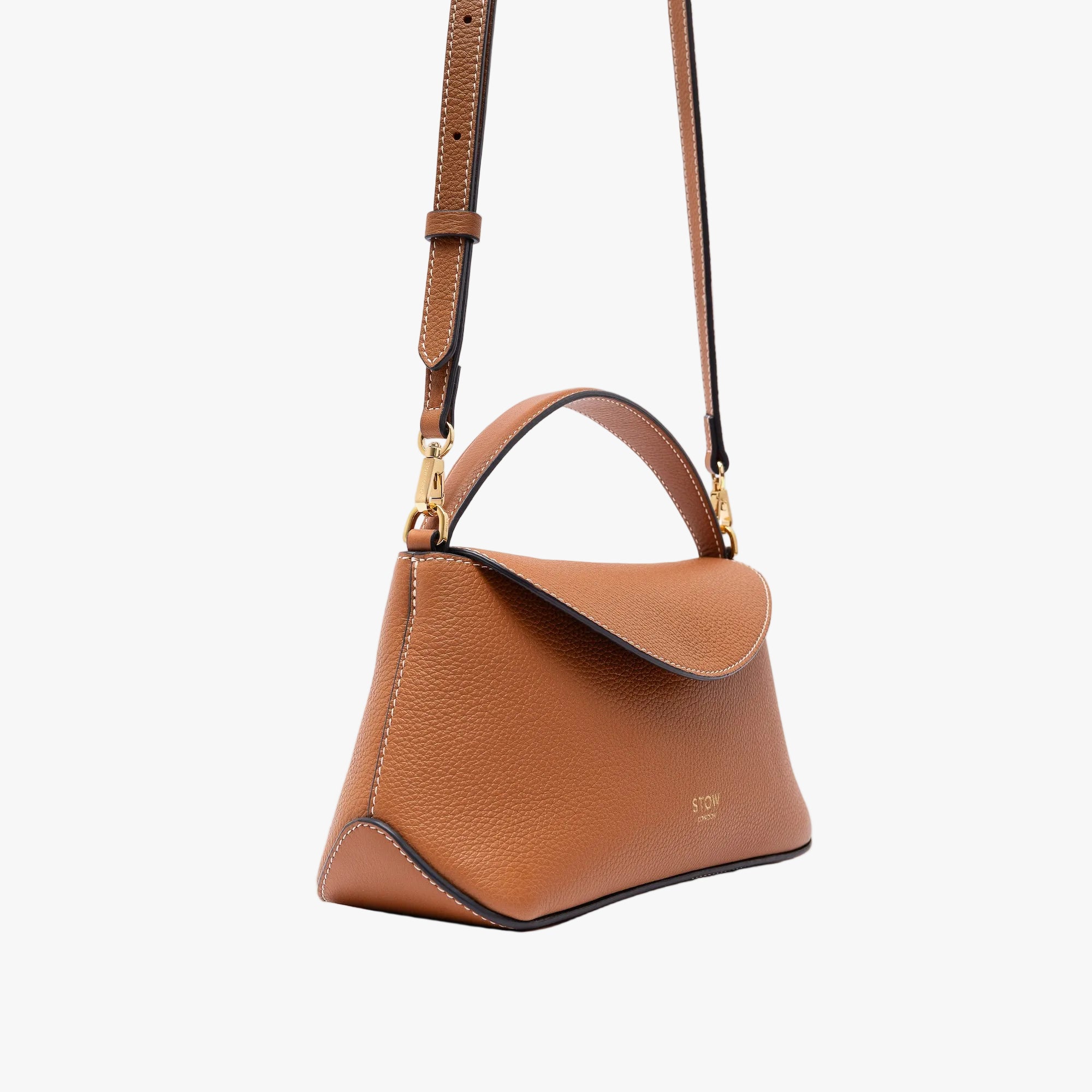 Off-axis view of STOW London's Mini East West in Earth Tan pebbled leather and detachable crossbody strap featuring gold-coated stainless steel hardware on a light grey background
