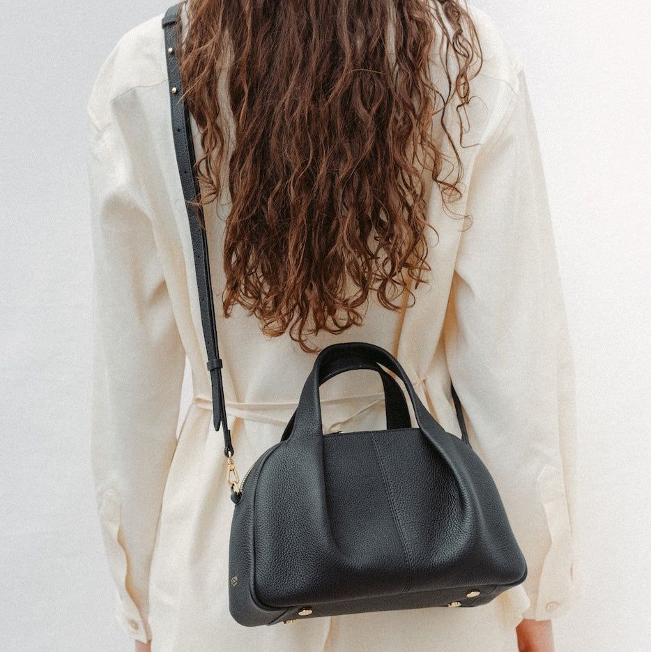 Model wearing STOW London's Mini Bowling in Black pebbled leather crossbody featuring a pleated front panel and gold-coated stainless steel hardware