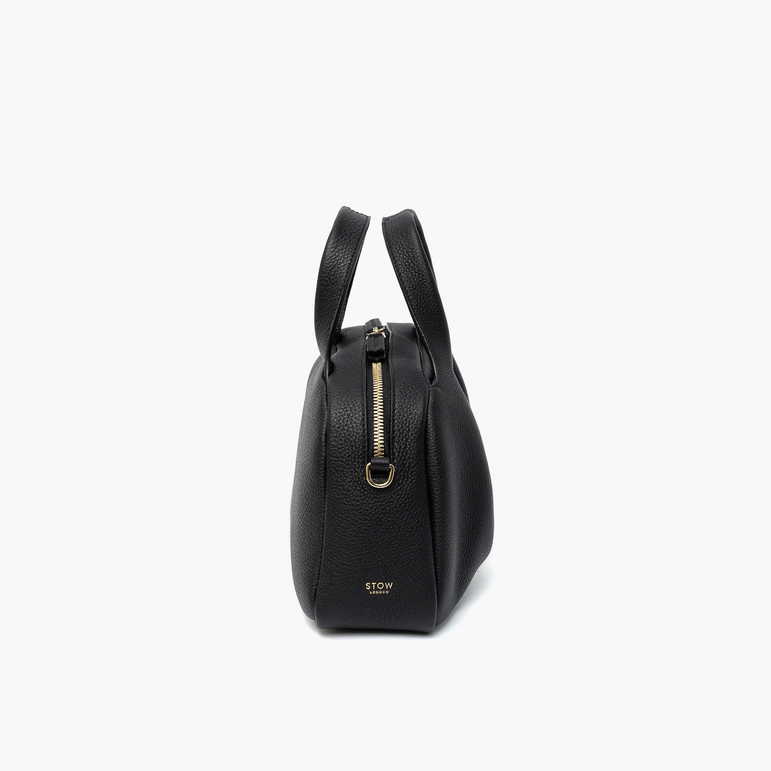 Side view of STOW London's Mini Bowling bag in Black pebbled leather featuring the zip closure, gold-coated stainless steel hardware and small logo on a light grey background