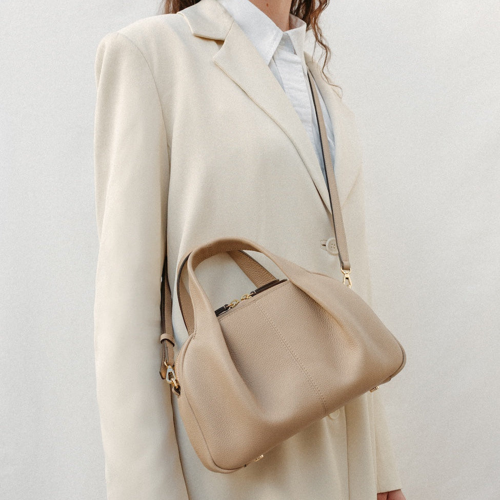 Model wearing STOW London's Mini Bowling bag in Camel pebbled leather crossbody featuring a pleated front panel, detachable crossbody strap and gold-coated stainless steel hardware
