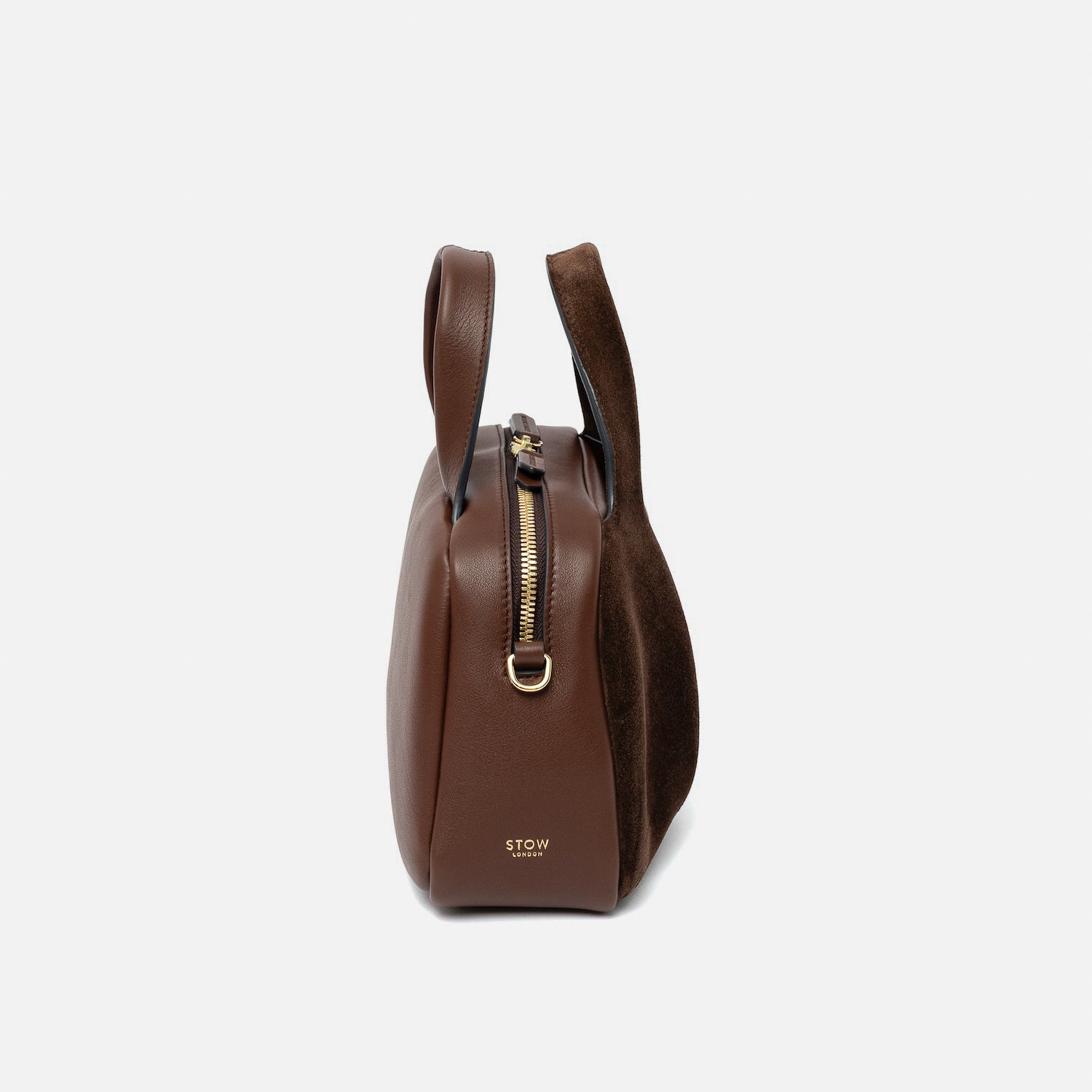 Side view of STOW London's Mini Bowling bag in Chocolate suede and smooth leather featuring the zip closure, gold-coated stainless steel hardware and small logo on a light grey background