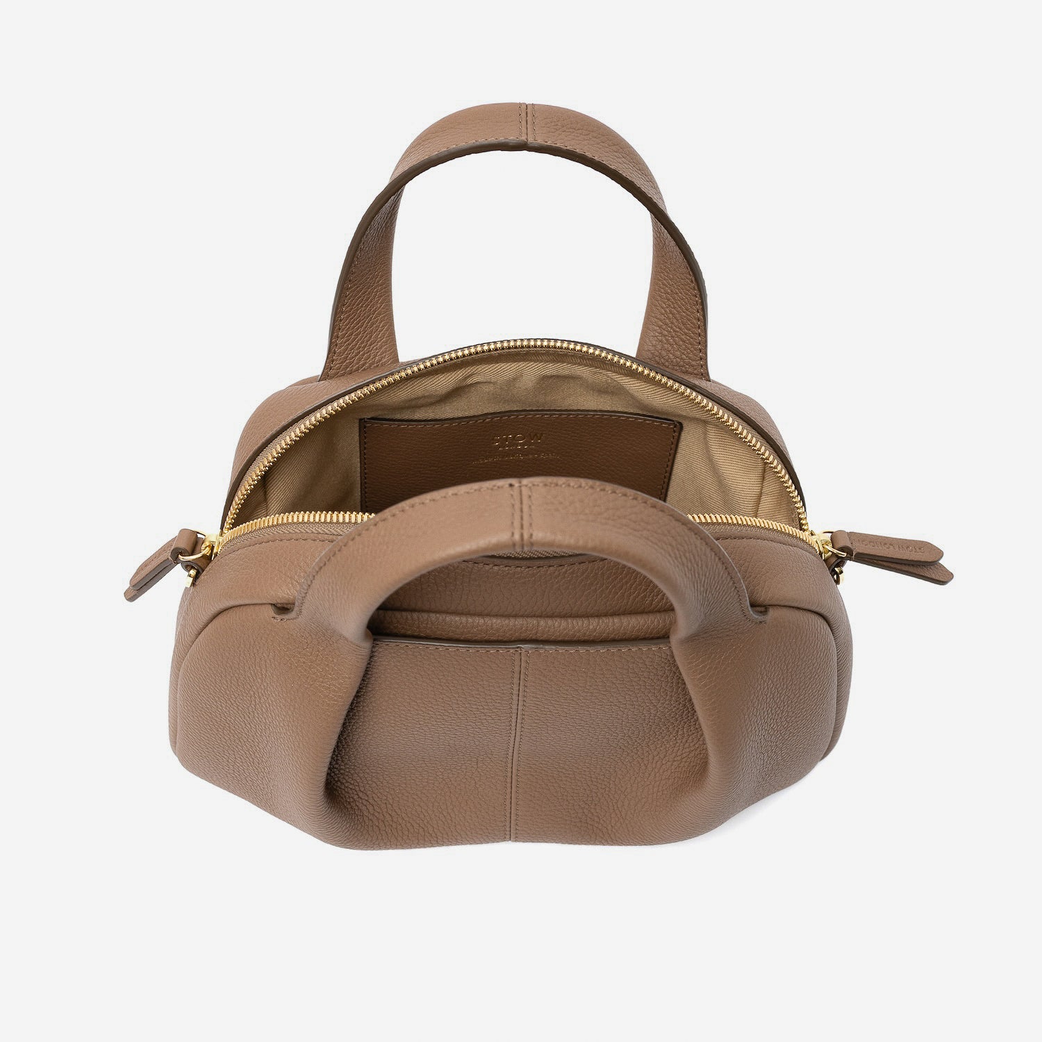 STOW London's Mini Bowling bag in Mocha pebbled leather with zip open showing the light beige interior lining and slip pocket featuring gold-coated stainless steel hardware on a light grey background