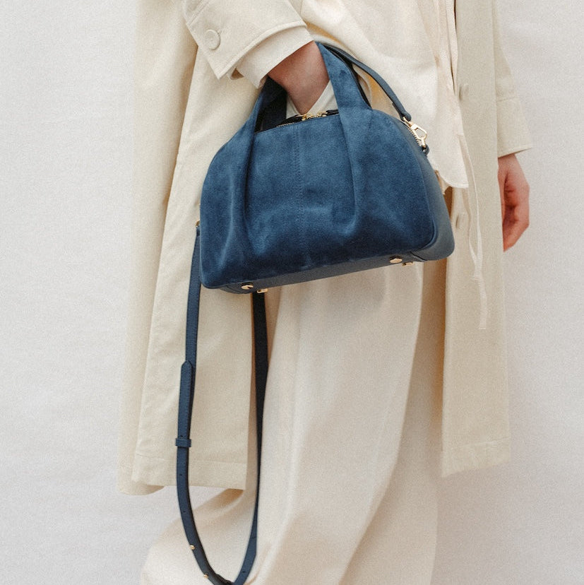 Model wearing STOW London's Mini Bowling in Navy suede leather on her wrist featuring a pleated front panel and gold-coated stainless steel hardware