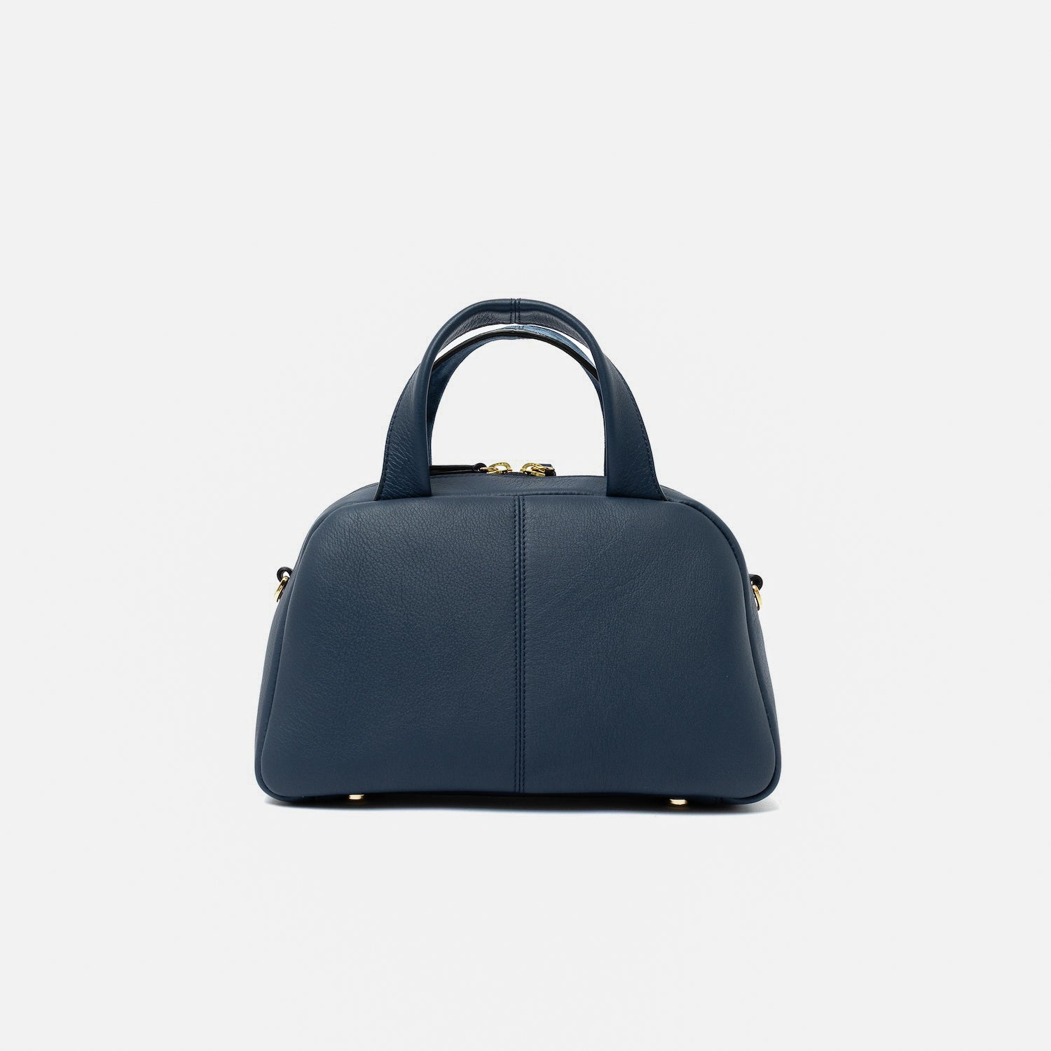 Shot of the smooth leather back panel of STOW London's Mini Bowling bag in Navy featuring gold-coated stainless steel hardware and four feet on the base on a light grey background