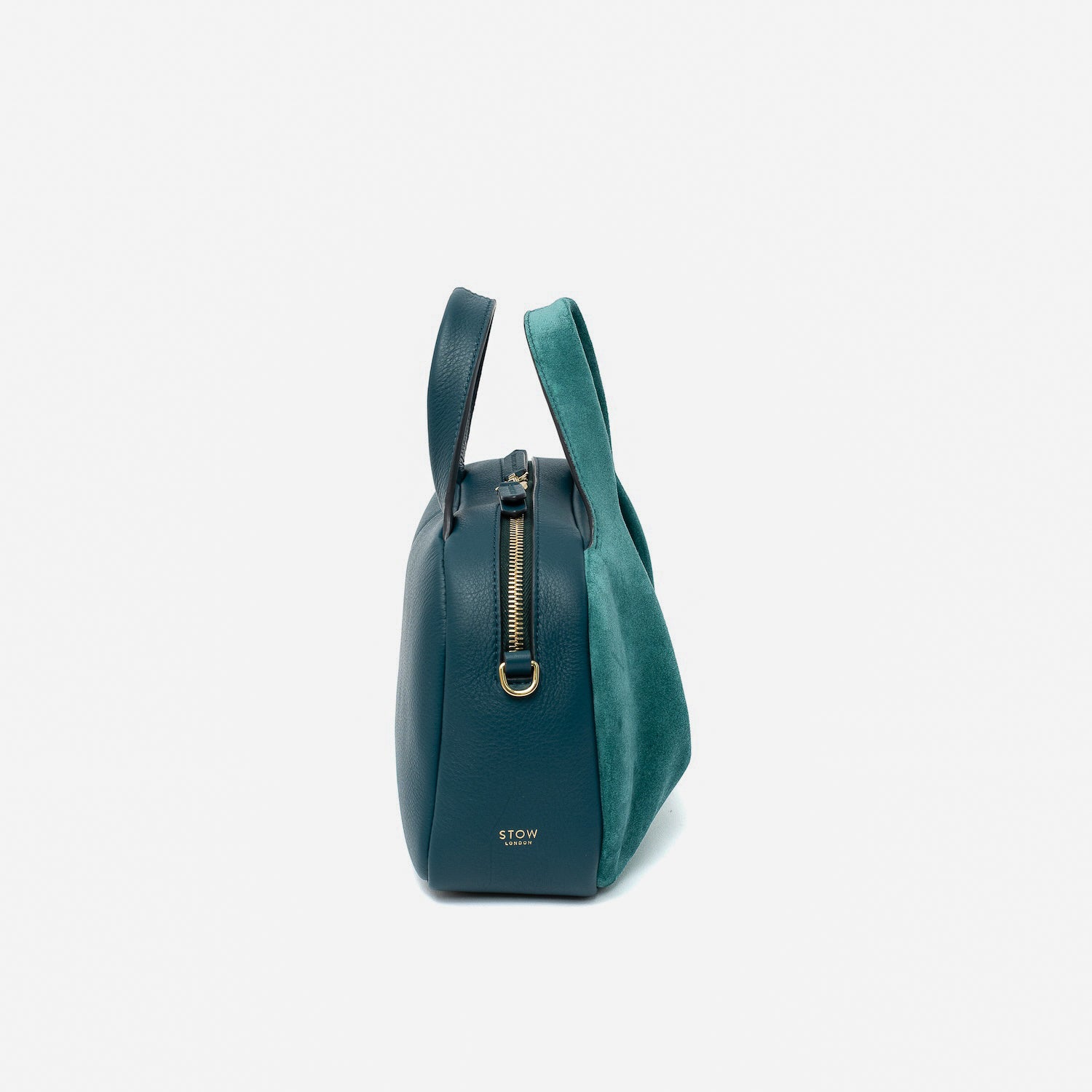 Side view of STOW London's Mini Bowling bag in Ocean Teal suede and smooth leather featuring a pleated front panel, gold-coated stainless steel hardware and small gold logo on a light grey background