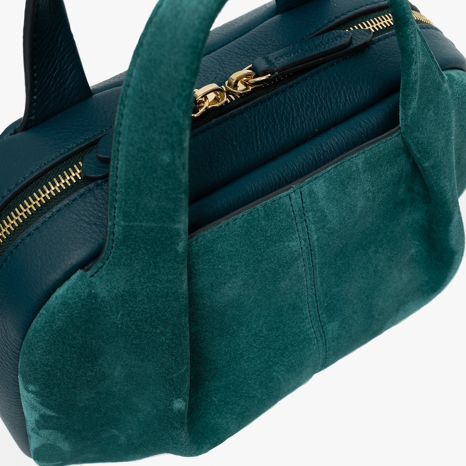 Close up of STOW London's Mini Bowling bag in Ocean Teal suede and smooth leather featuring a pleated front panel, the zip closure with STOW London embossed pull tabs on a light grey background
