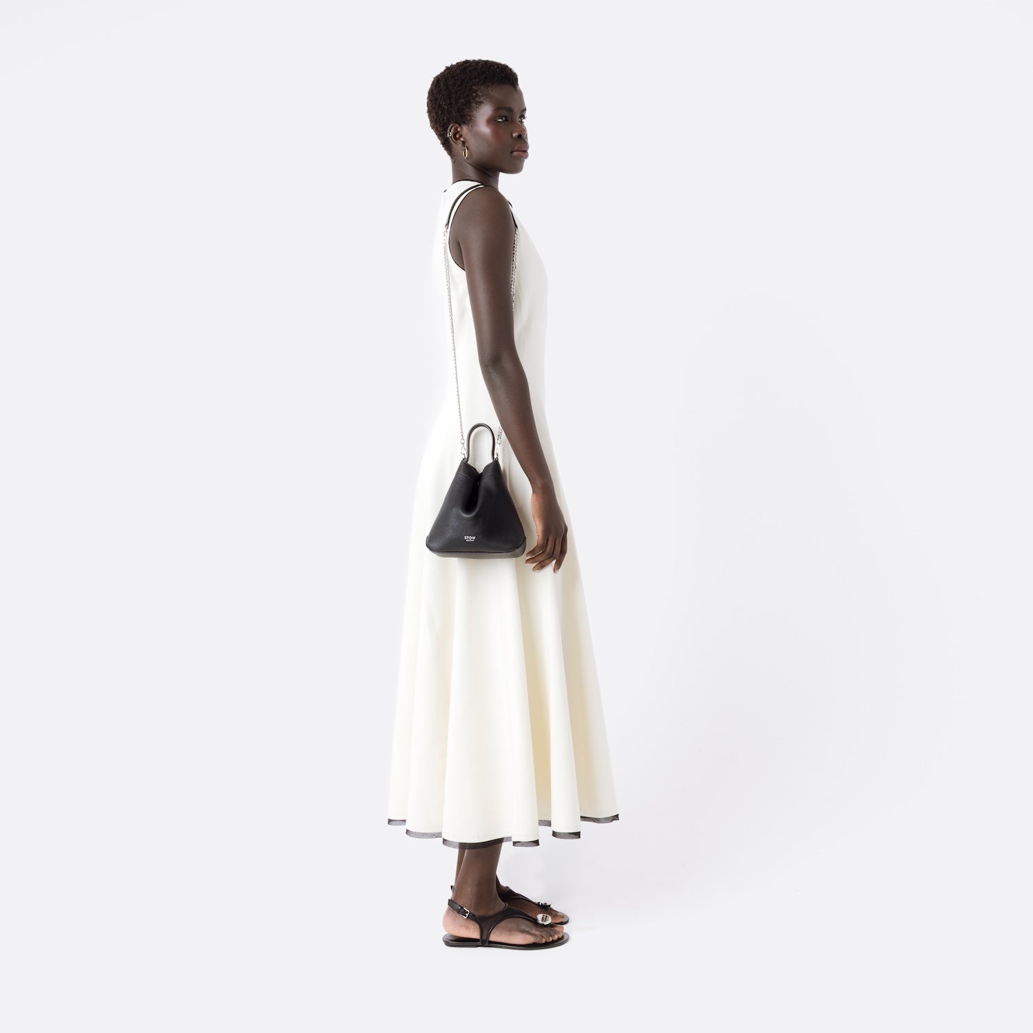 Model wearing Stow London's Mini Curve in Black pebbled leather on her shoulder by the detachable silver chain crossbody strap on a white background
