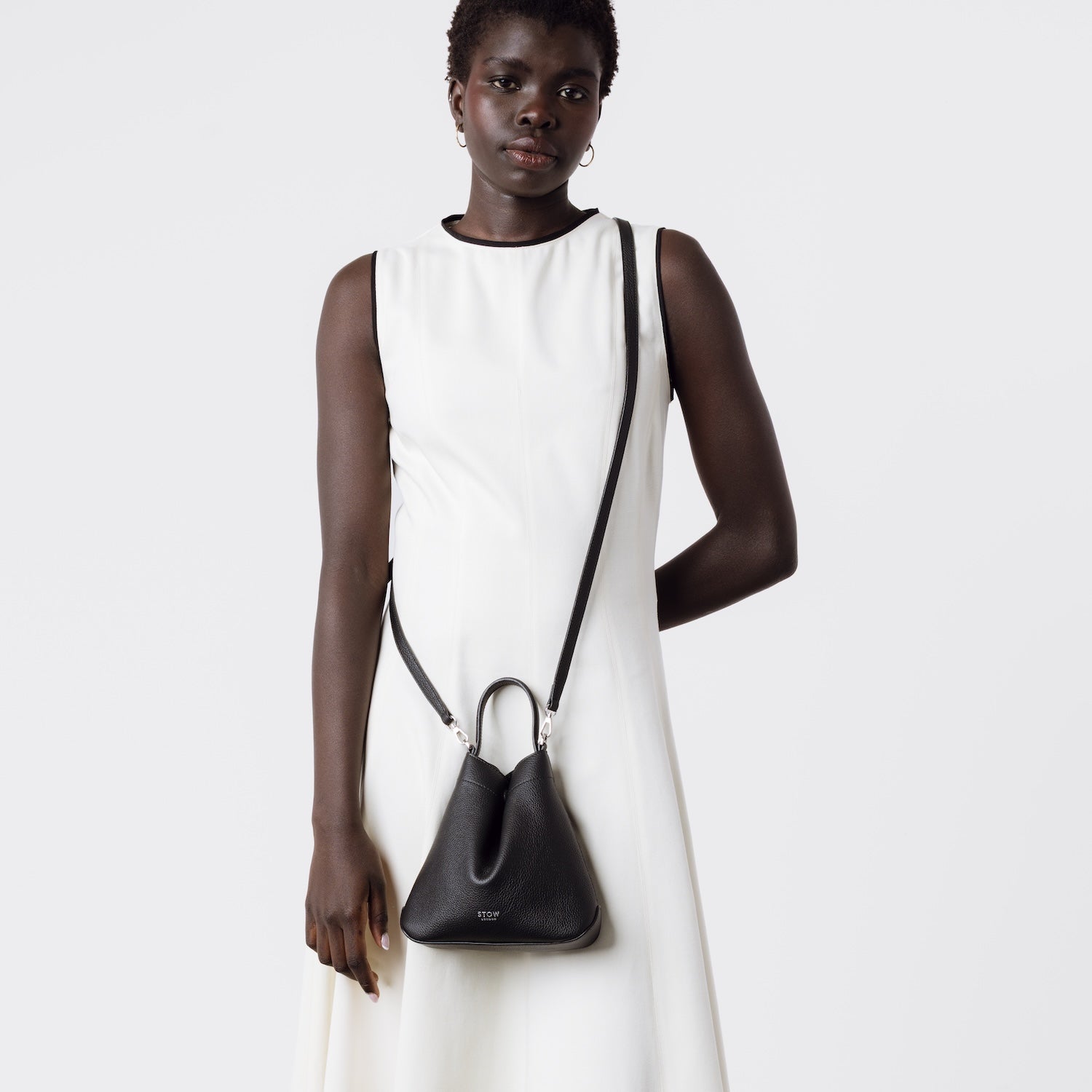 Model wearing STOW London's Mini Curve in Black pebbled leather with the detachable leather crossbody strap on a white background