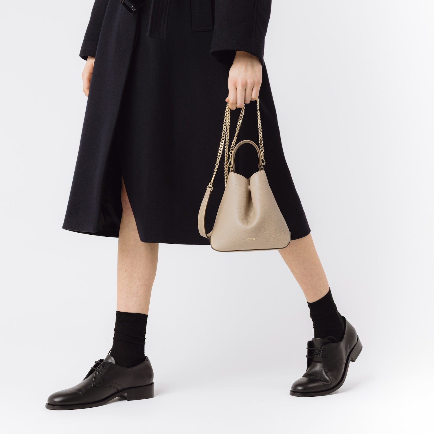 STOW London's Mini Curve in Camel leather held by model by the gold-plated chain on a white background