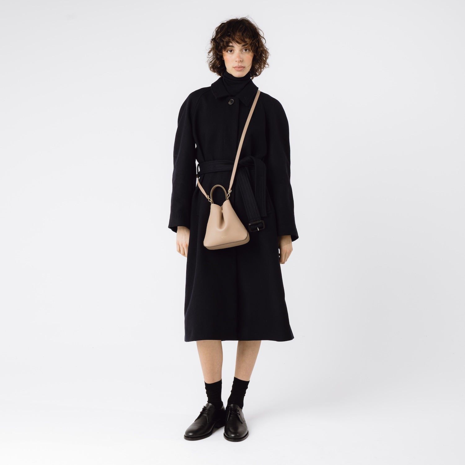 STOW London's Mini Curve and leather crossbody strap in Camel worn crossbody on model, on a white background