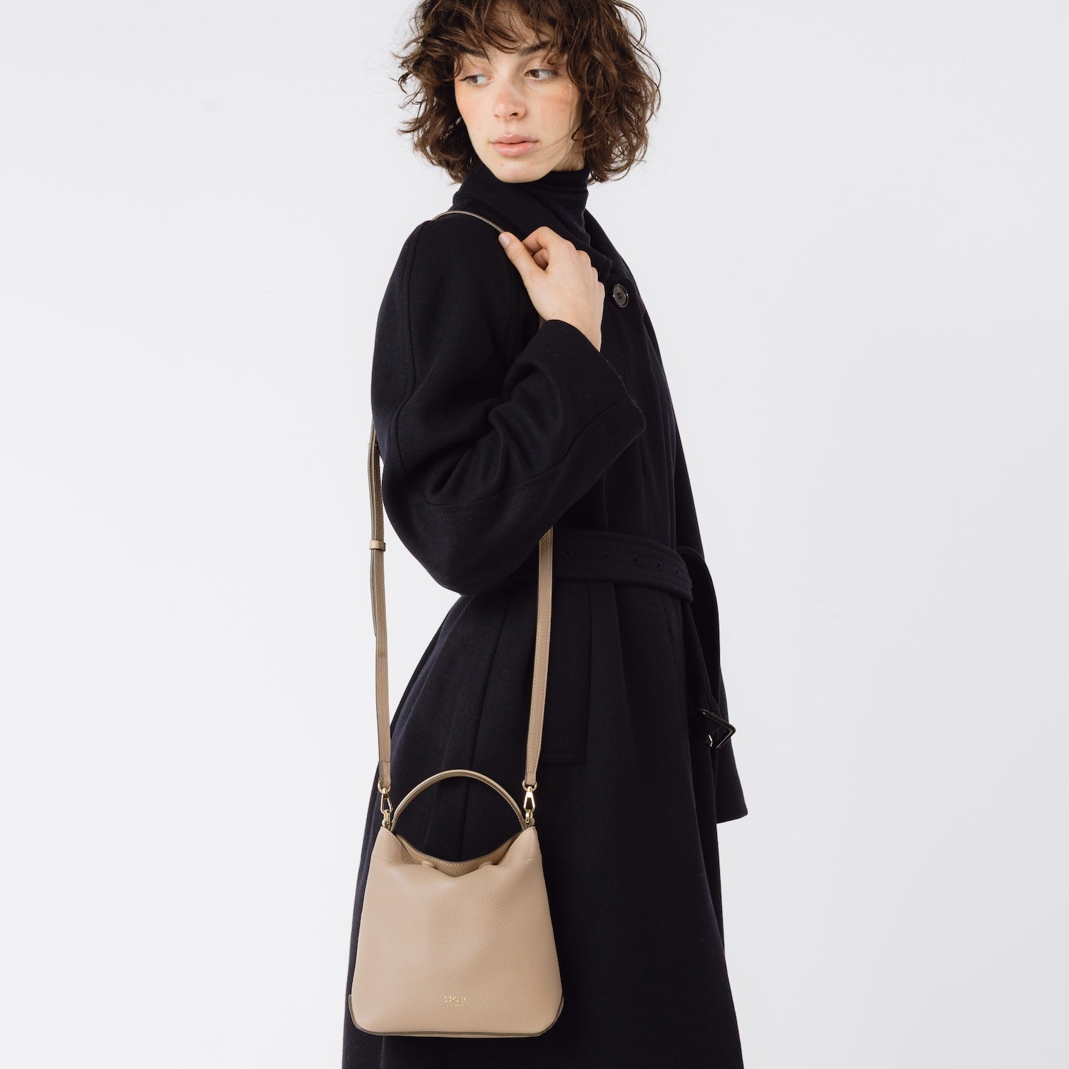 STOW London's Mini Curve and leather crossbody strap in Camel worn over model's shoulder featuring gold-coated stainless steel hardware on a white background