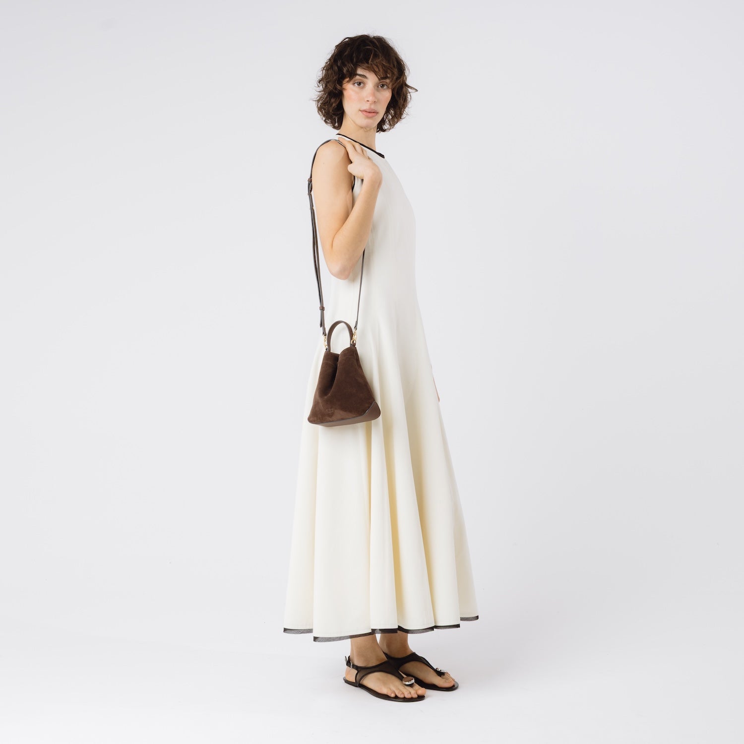 Model wearing STOW London's Mini Curve in Chocolate suede leather with the detachable leather crossbody strap on her shoulder on a white background