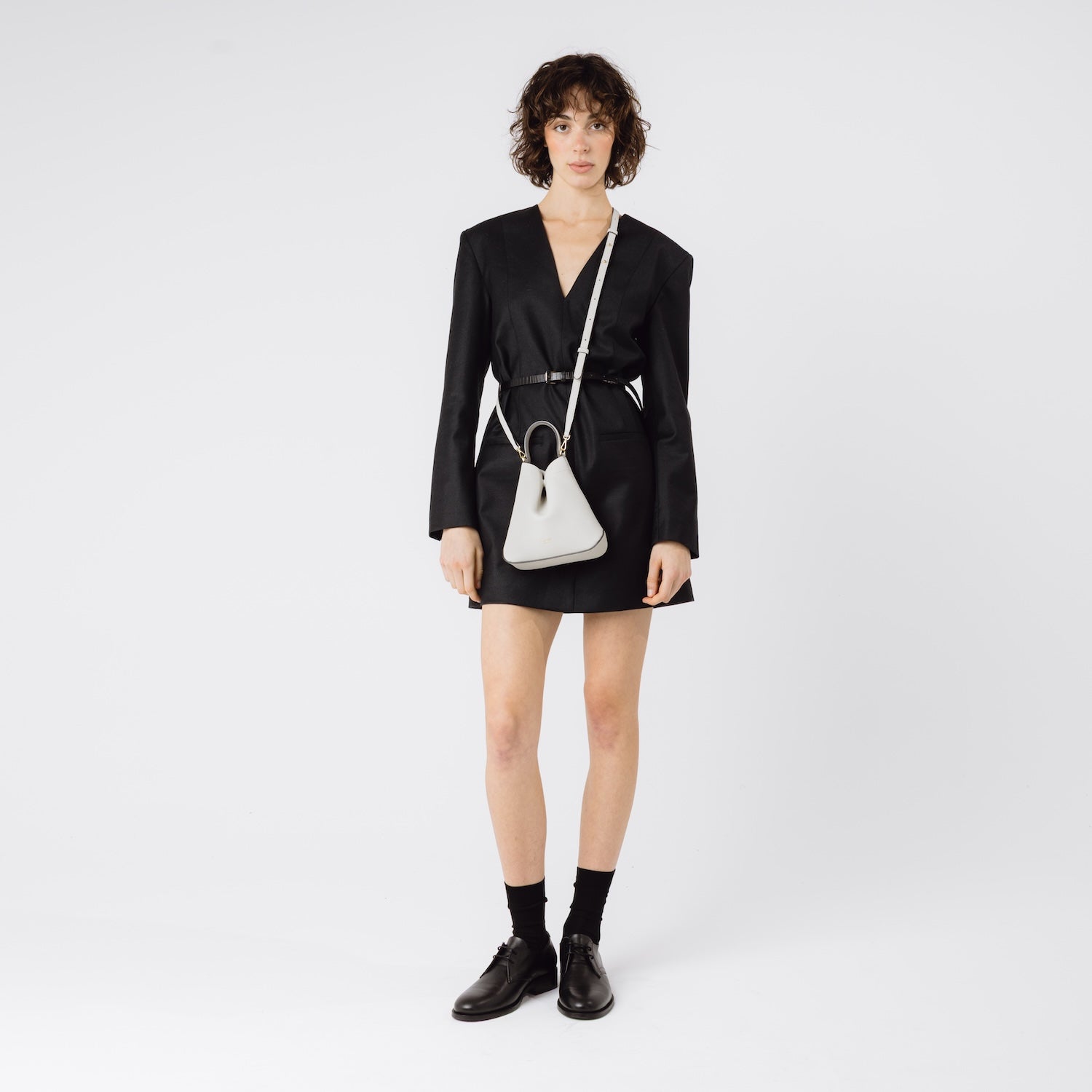 Model wearing STOW London's Mini Curve in Cloud Grey pebbled leather with the detachable leather crossbody strap on a white background