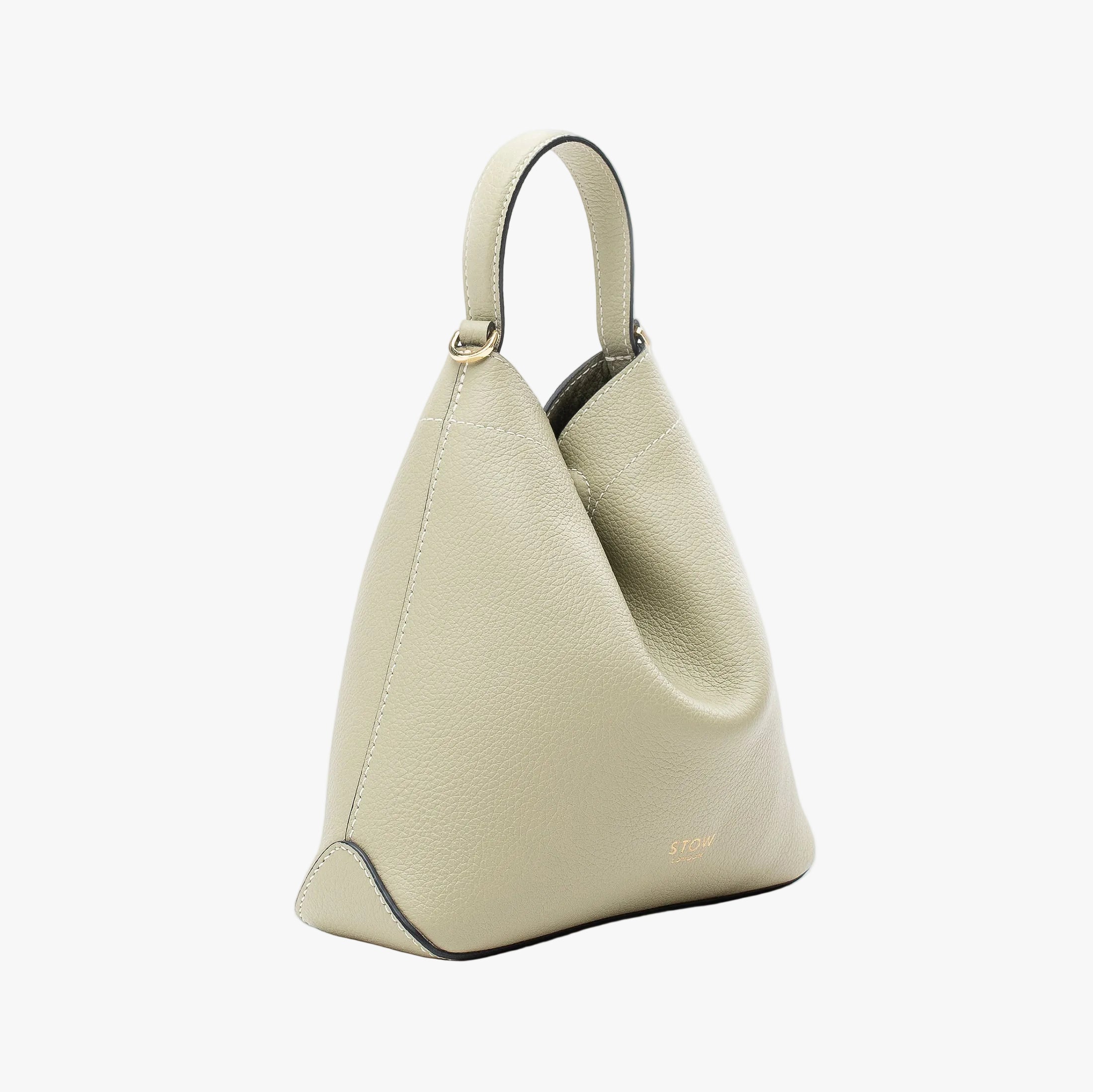 Off-axis view of STOW London's Mini Curve in Pale Green pebbled leather featuring gold details on a light grey background