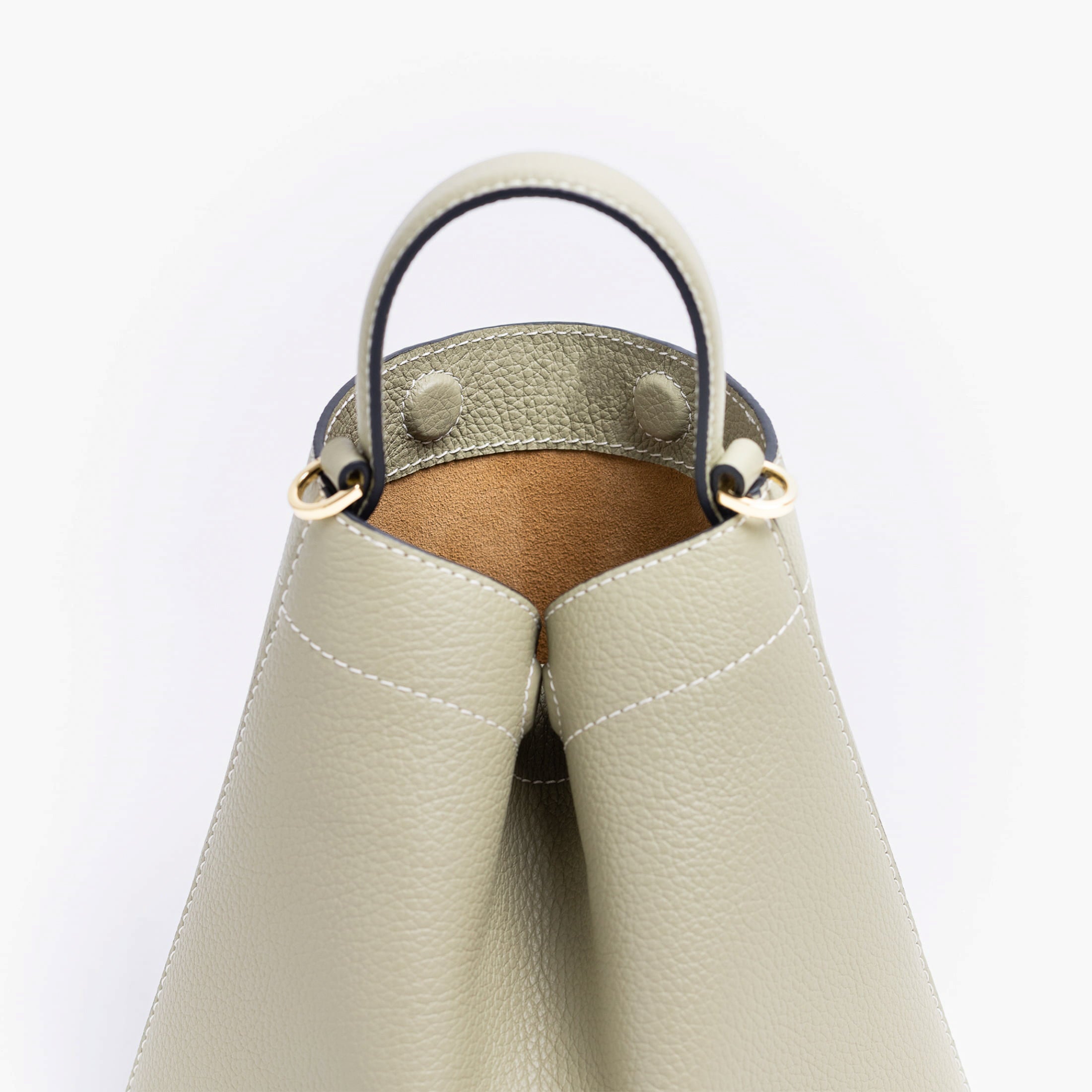 Close up of STOW London's Mini Curve in Pale Green pebbled leather featuring hidden magnets, suede lining and gold hardware on a light grey background