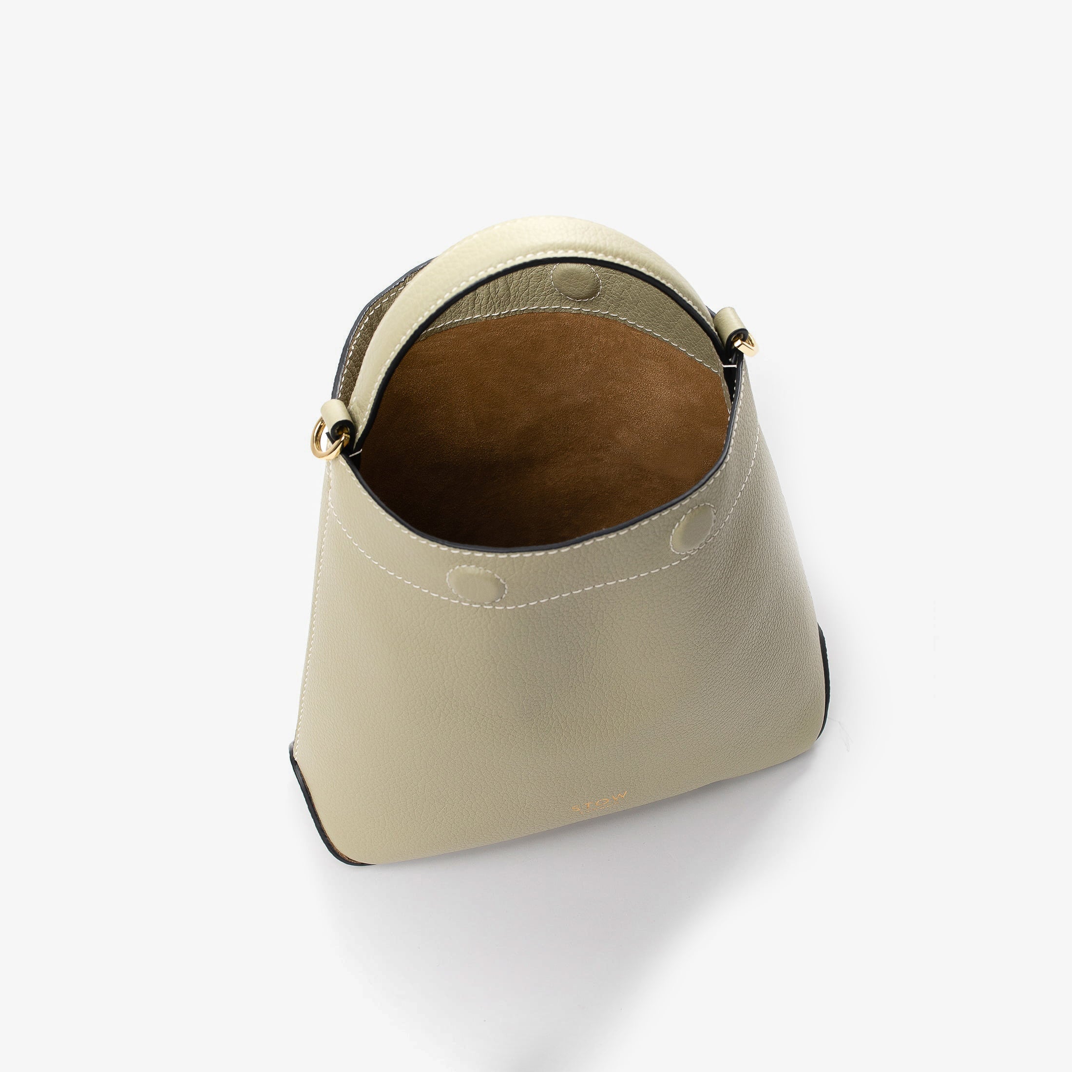 Top view of STOW London's Mini Curve in Pale Green pebbled leather with magnets open showing cognac suede interior lining on a light grey background