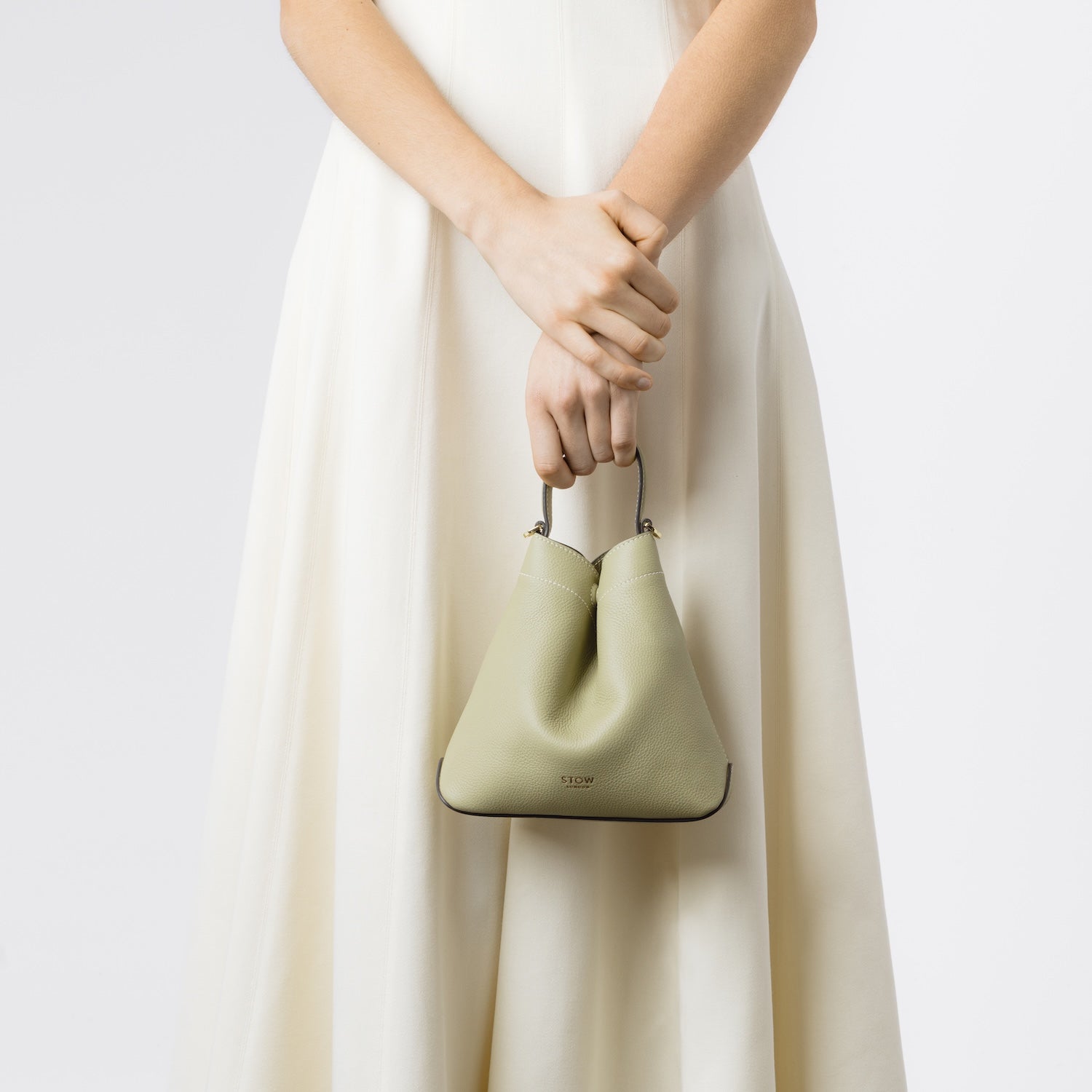 Model holding STOW London's Mini Curve in Pale Green pebbled leather by top handle on a white background