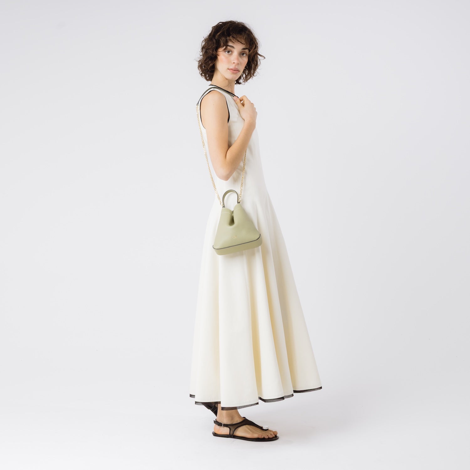 Model wearing STOW London's Mini Curve in Pale Green pebbled leather on he shoulder by detachable gold chain crossbody strap on a white background