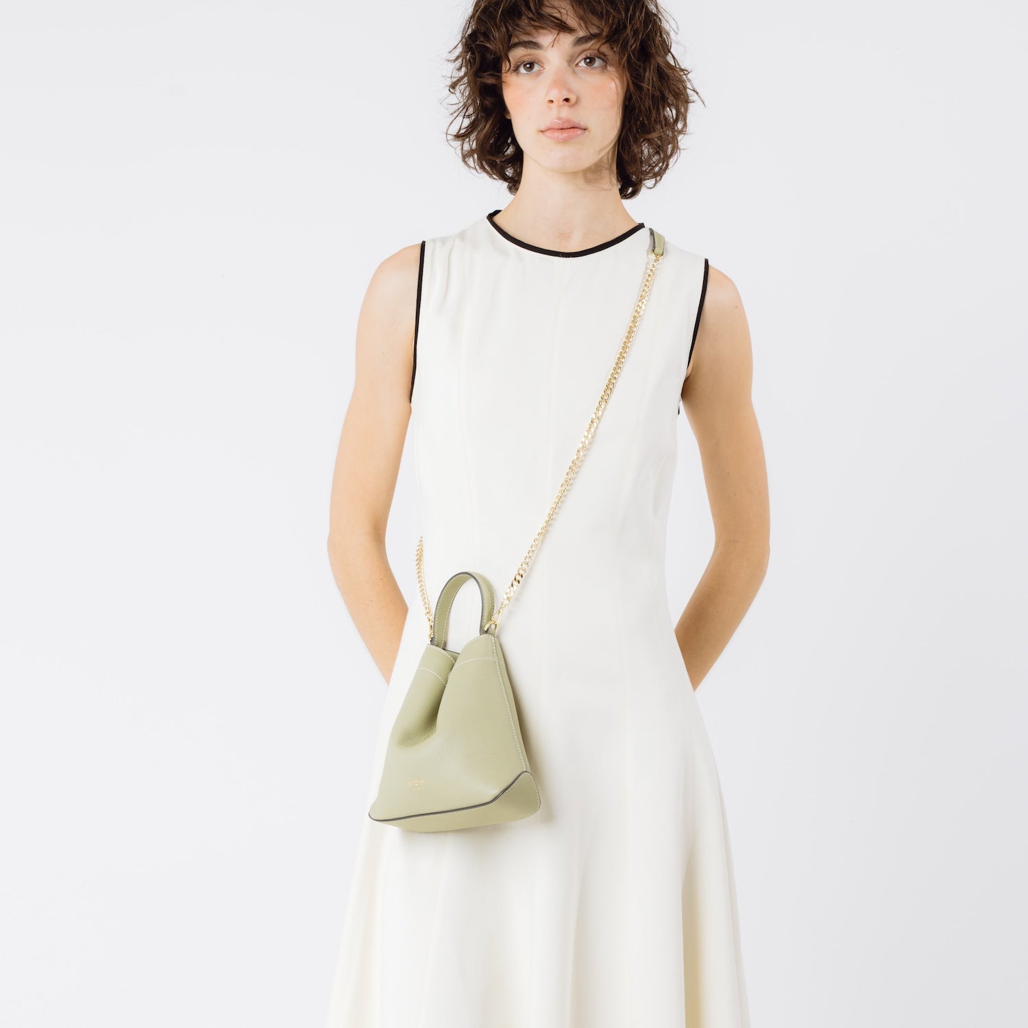 Model wearing STOW London's Mini Curve in Pale Green pebbled leather crossbody with gold-plated chain strap on a white background