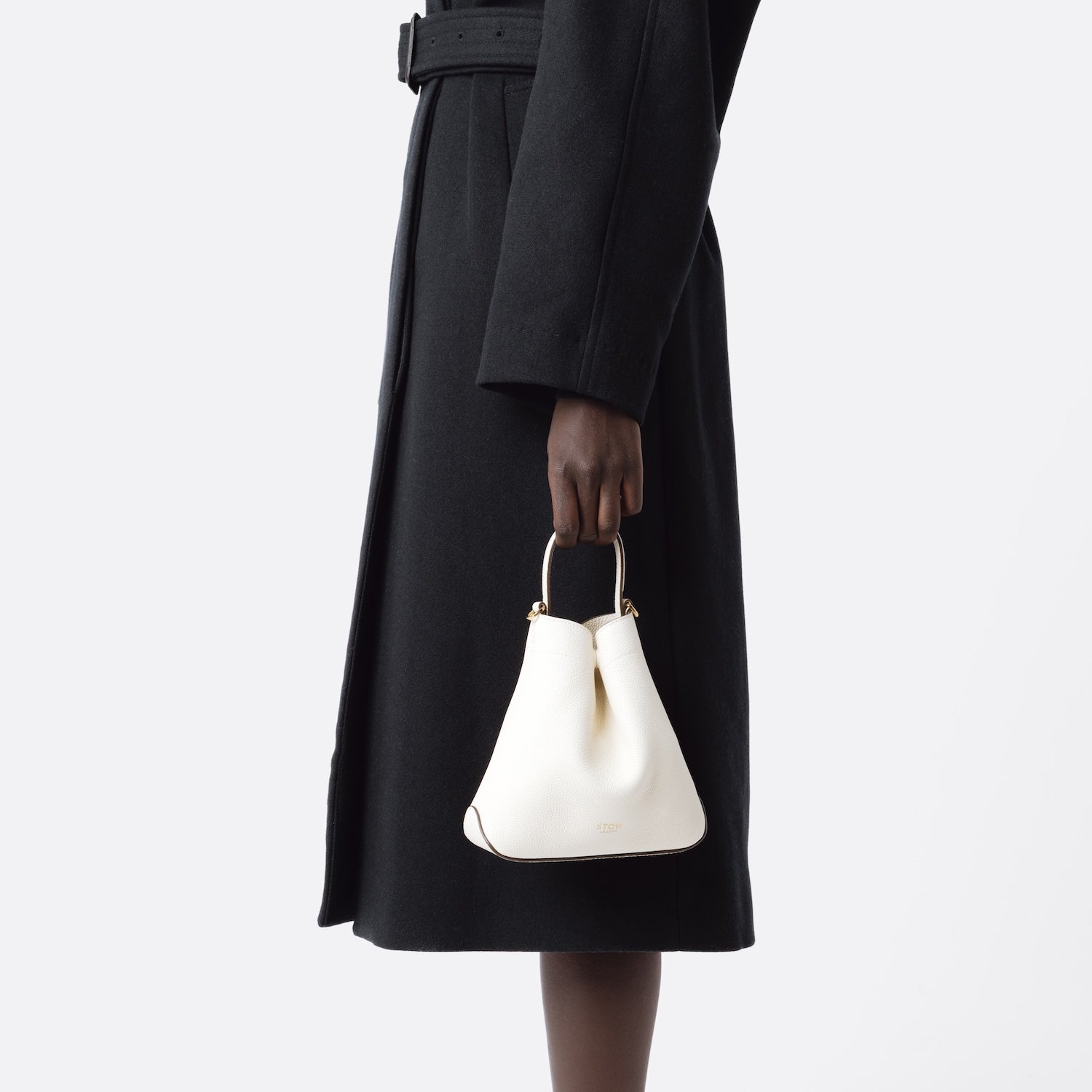 Model holding STOW London's Mini Curve in Spring Moon pebbled leather featuring gold details on a white background