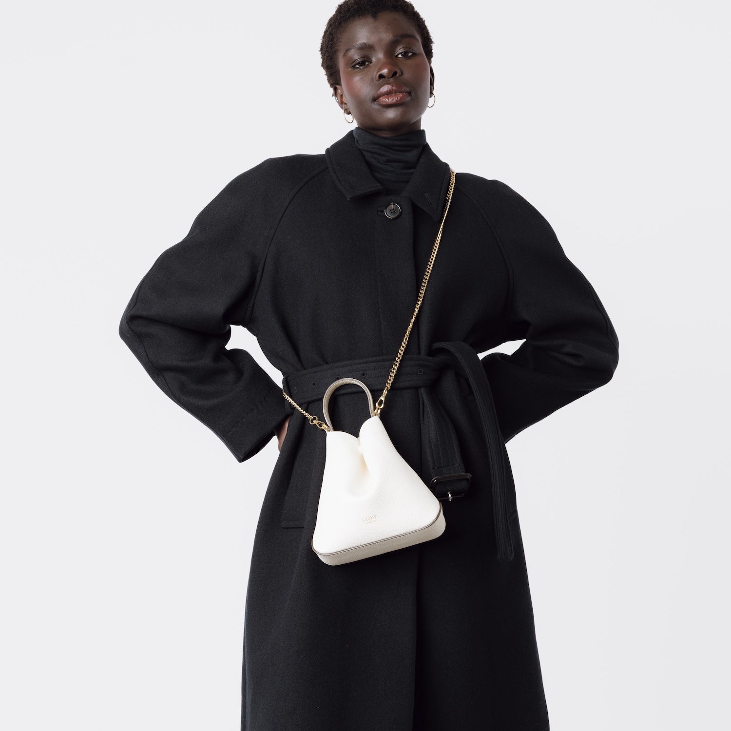 Model wearing STOW London's Mini Curve in Spring Moon pebbled leather crossbody by gold chain strap on a white background