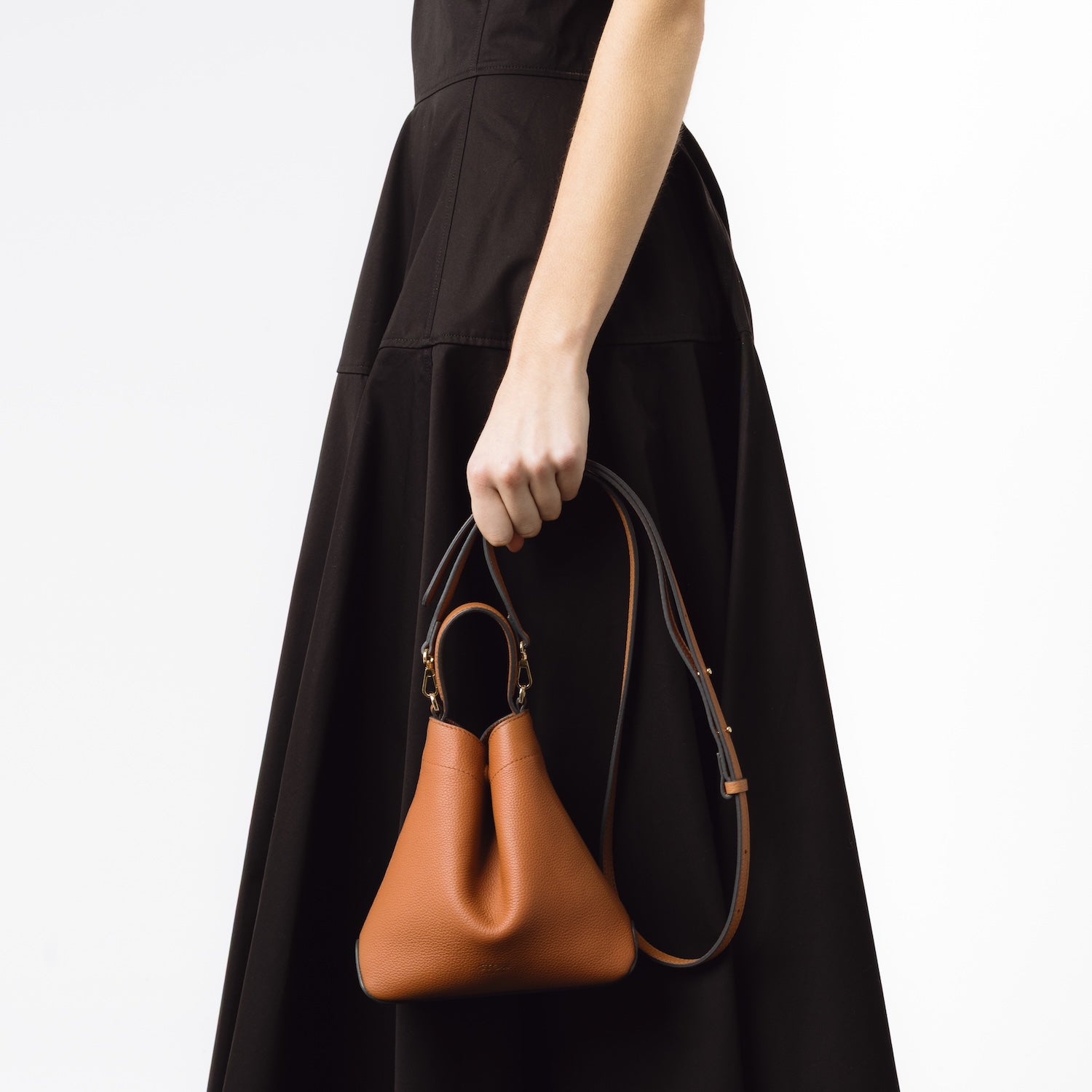 STOW London's Mini Curve in Earth Tan held by model by detachable leather crossbody strap featuring gold-coated stainless steel hardware on a white background