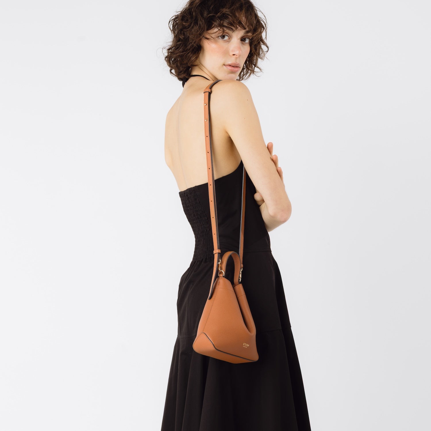 STOW London's Mini Curve in Earth Tan worn on shoulder by detachable leather strap featuring gold-coated stainless steel hardware on a white background