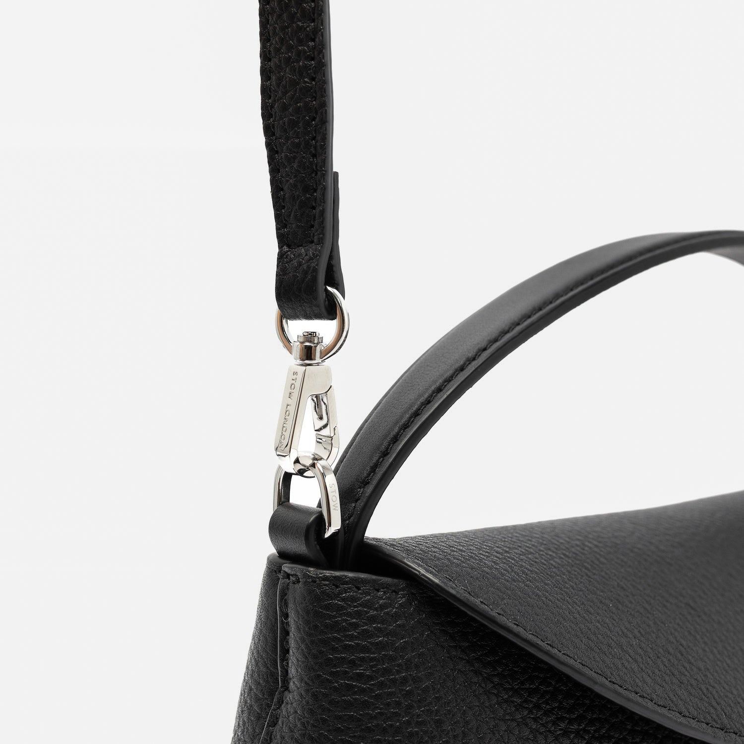 Close up of the detachable crossbody strap clip of STOW London's Mini East West in Black pebbled leather featuring silver stainless steel hardware on a light grey background