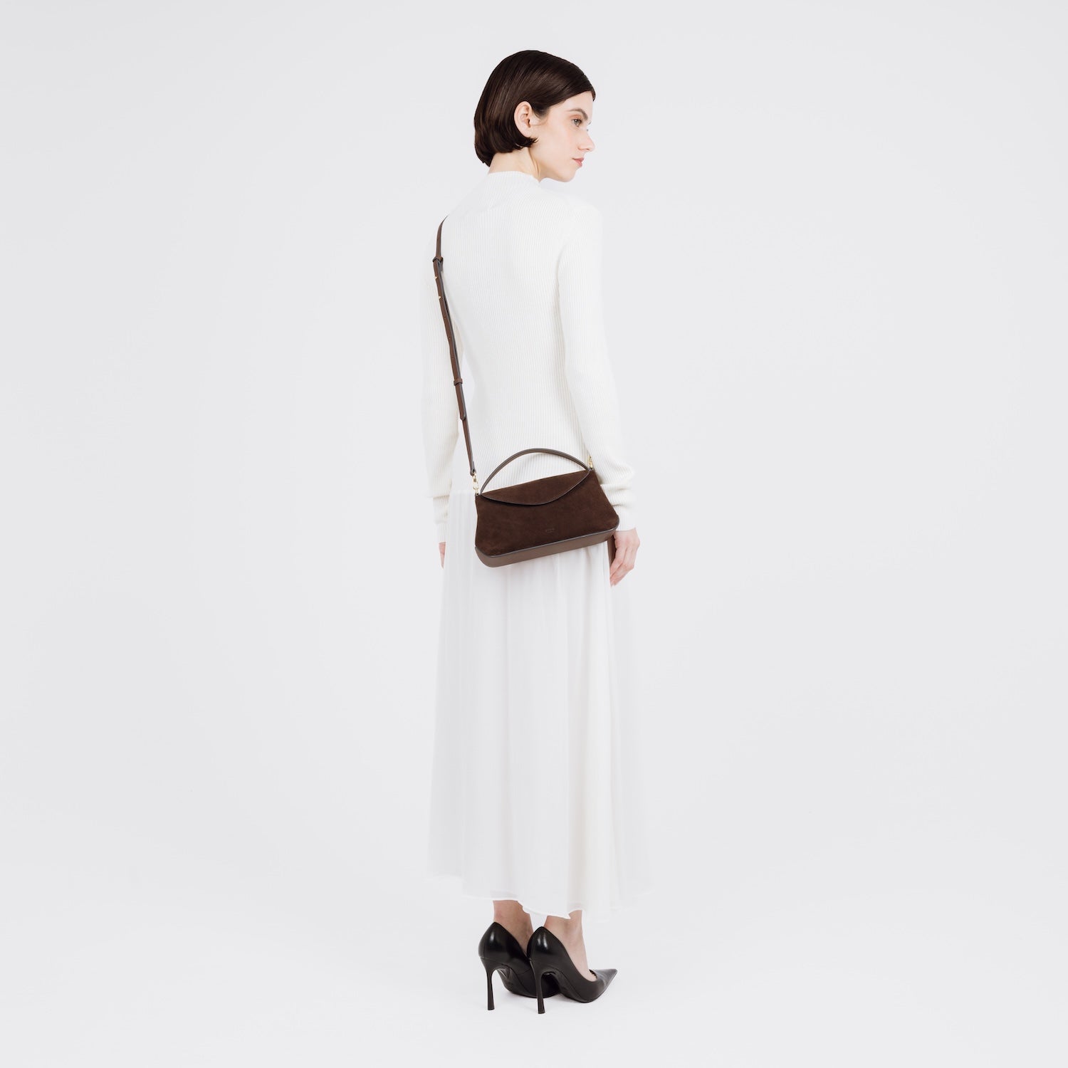 Model wearing STOW London's Mini East West bag in Chocolate Suede leather crossbody featuring gold-coated stainless steel hardware on a white background
