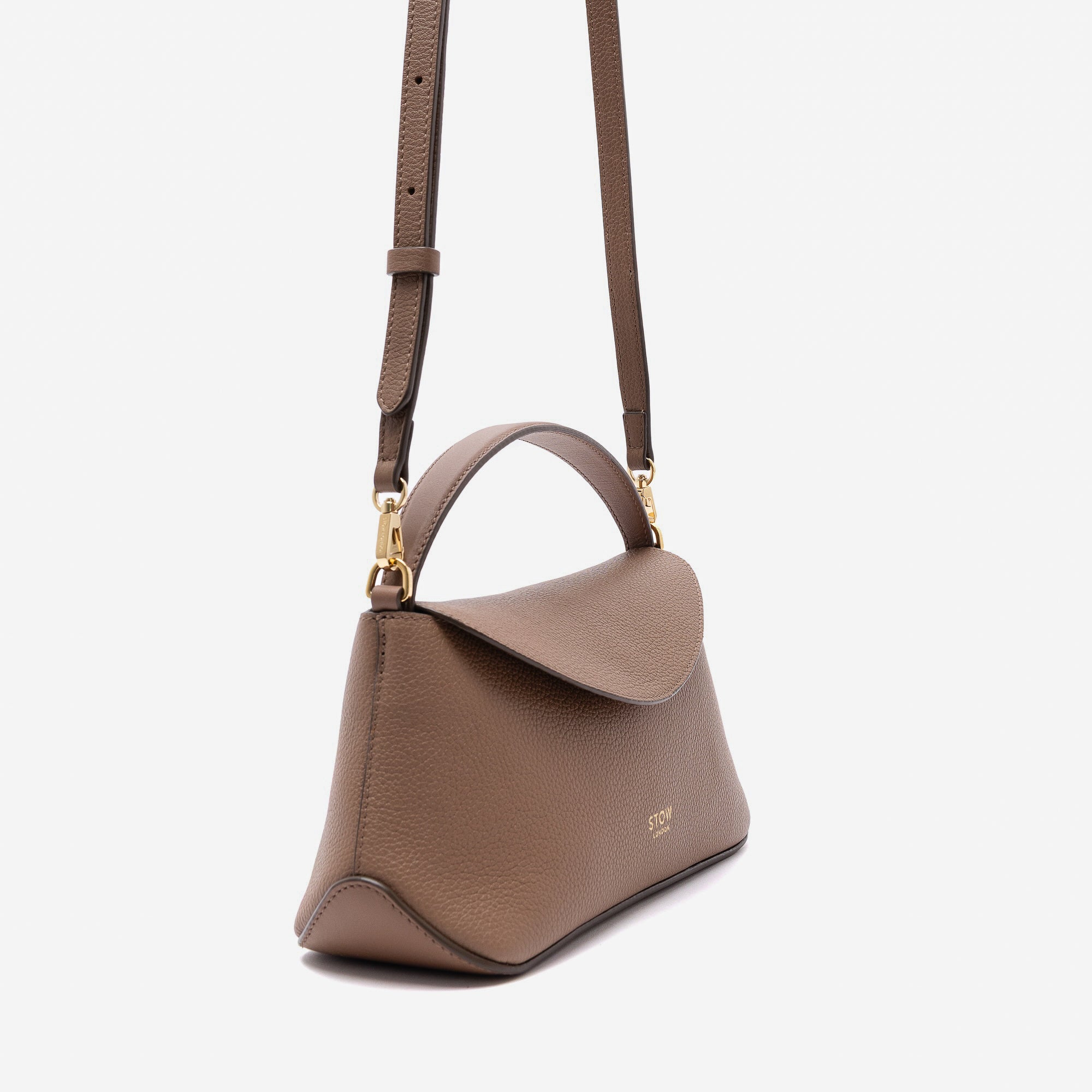 Off-axis view of STOW London's Mini East West in Mocha pebbled leather and detachable crossbody strap featuring gold-coated stainless steel hardware on a light grey background