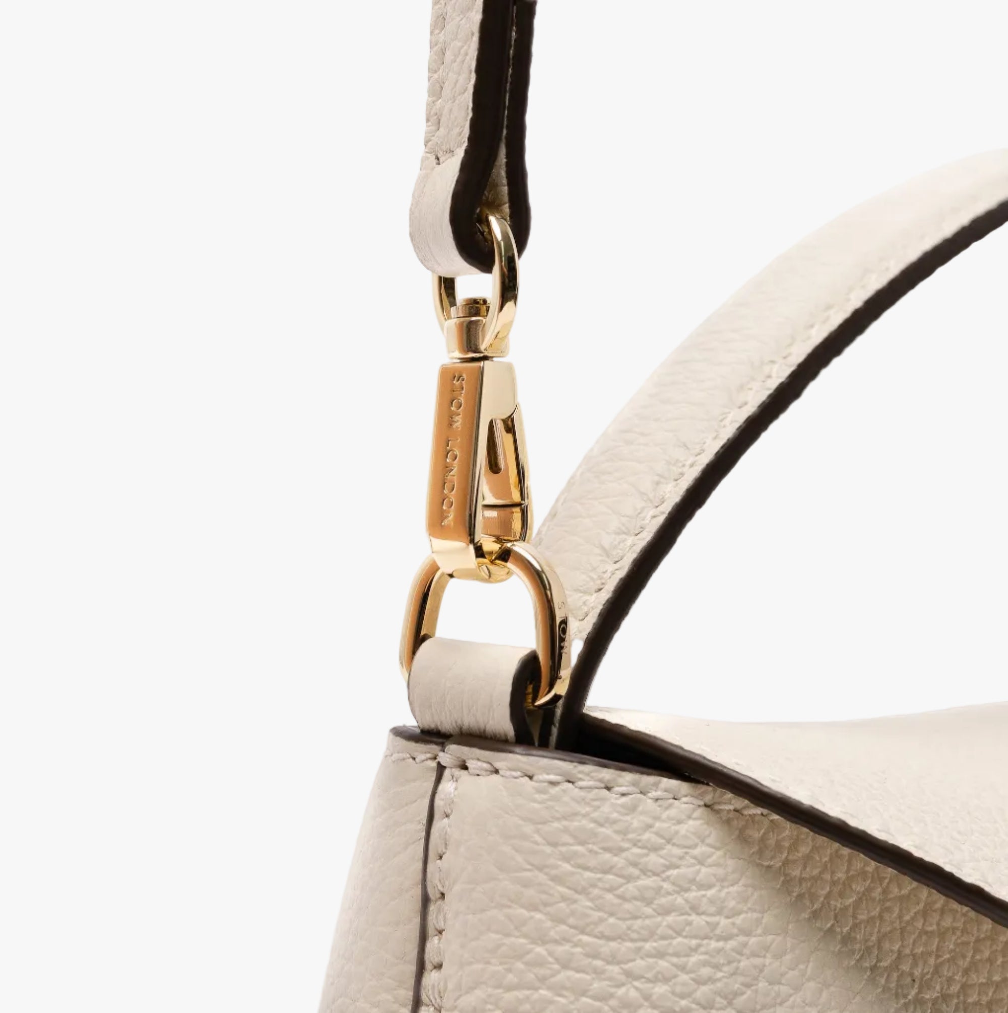 Close up of the detachable crossbody strap clip of STOW London's Mini East West in Spring Moon pebbled leather featuring gold-coated stainless steel hardware on a light grey background