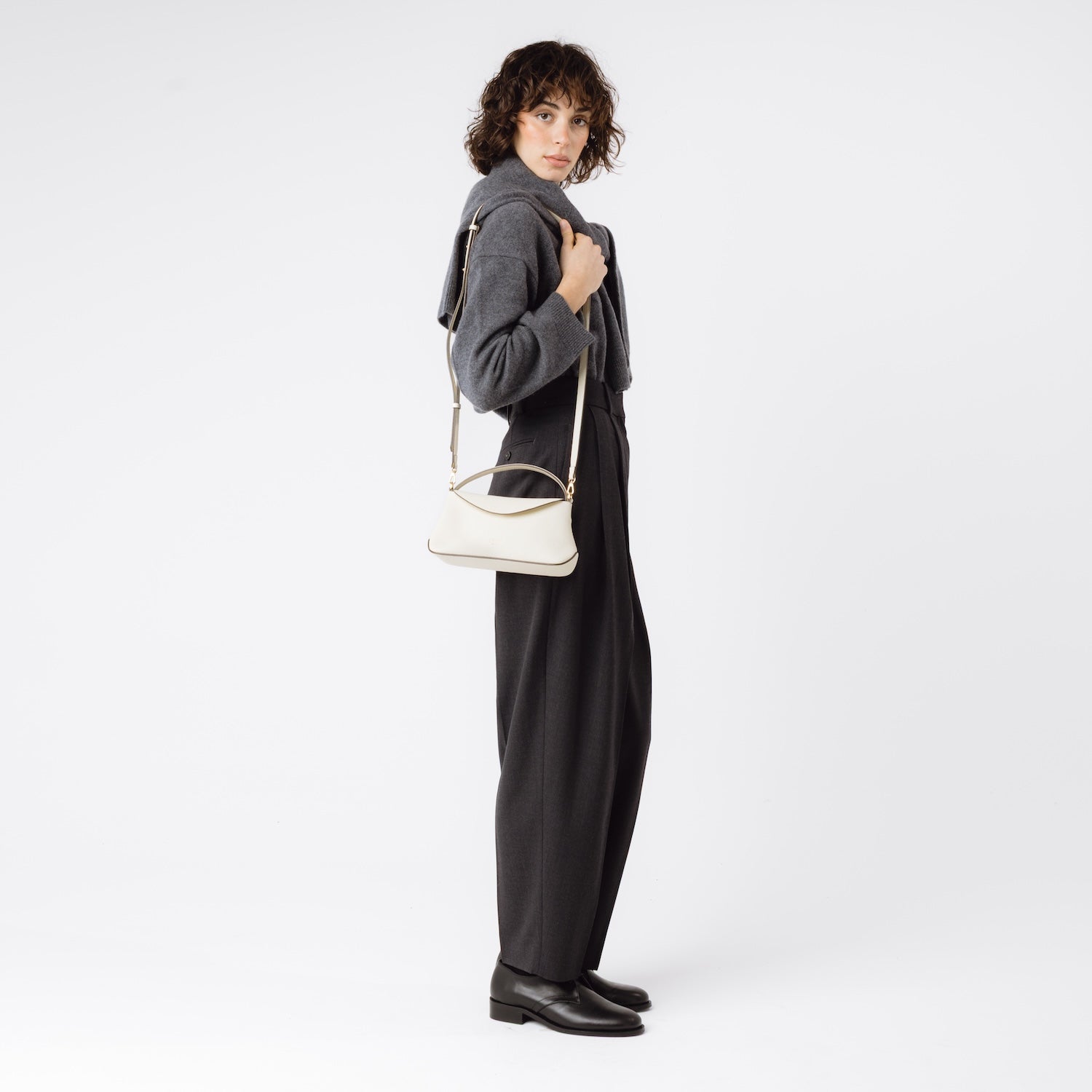 Model wearing STOW London's Mini East West in Spring Moon pebbled leather on her shoulder featuring gold-coated stainless steel hardware on a white background