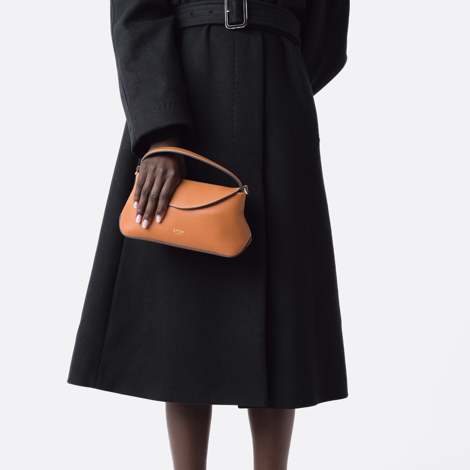 Model holding STOW London's Earth Tan Mini East West bag featuring gold-coated stainless steel hardware on a white background