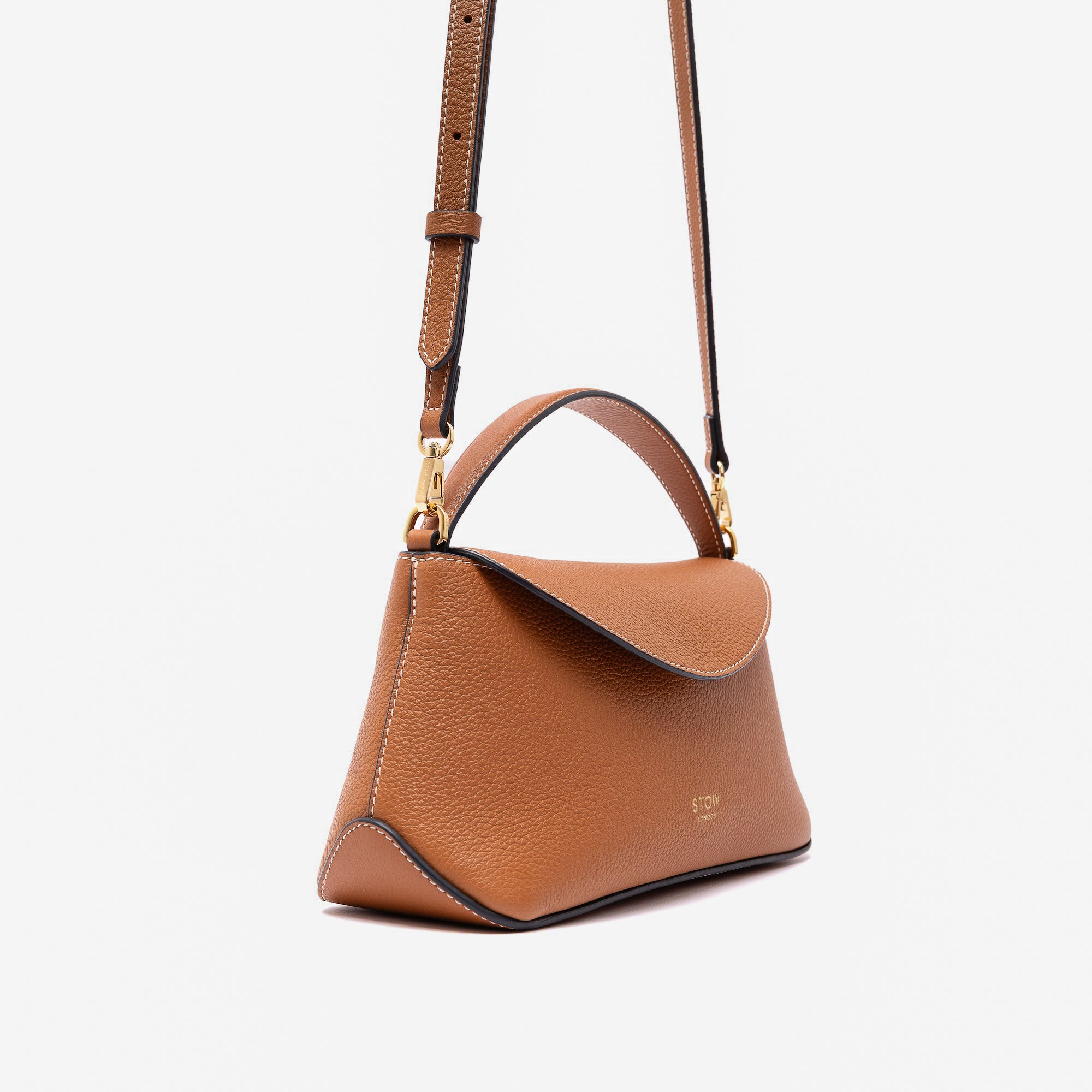 Off-axis view of STOW London's Mini East West in Earth Tan pebbled leather and detachable crossbody strap featuring gold-coated stainless steel hardware on a light grey background
