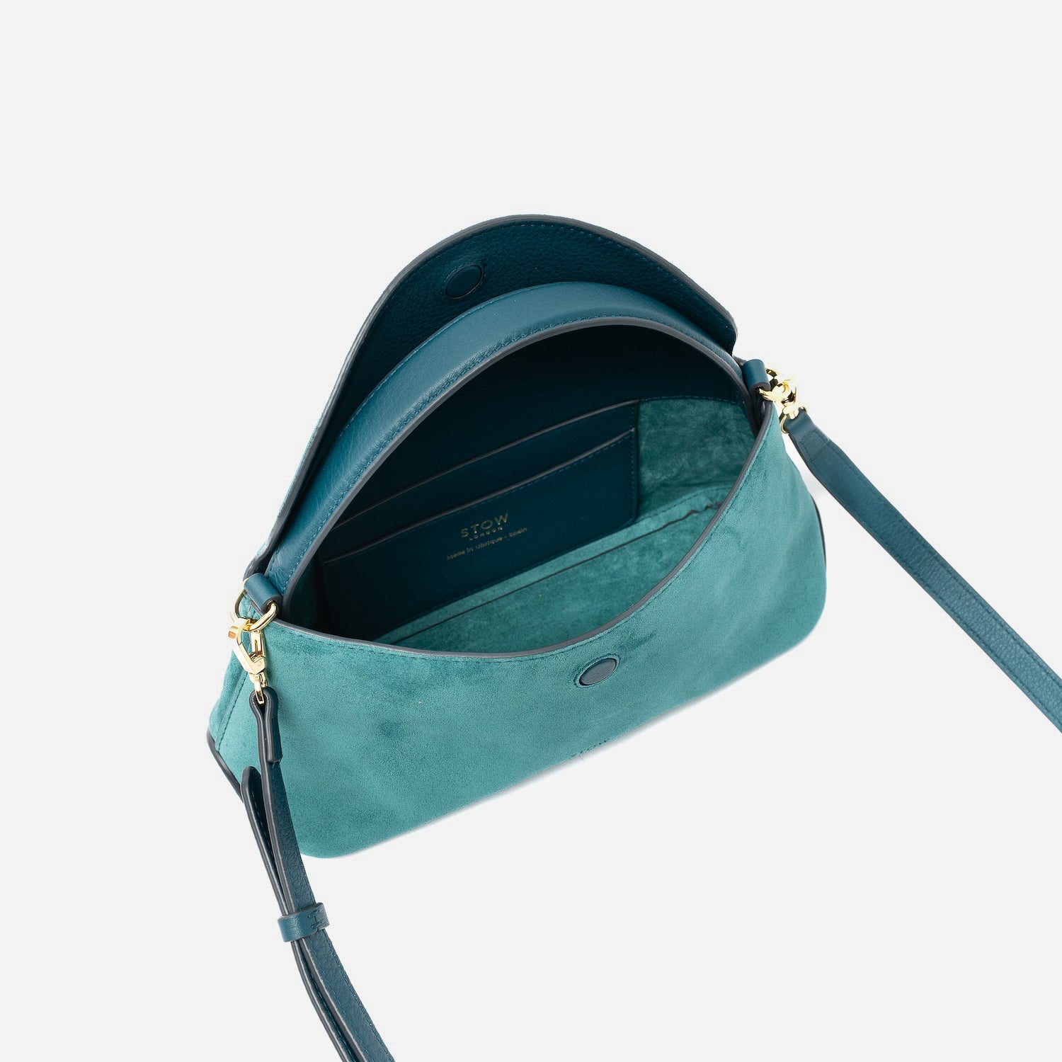 STOW London's Mini East West in Ocean Teal suede leather with flap open showing suede interior and slip pocket featuring gold-coated stainless steel hardware on a light grey background