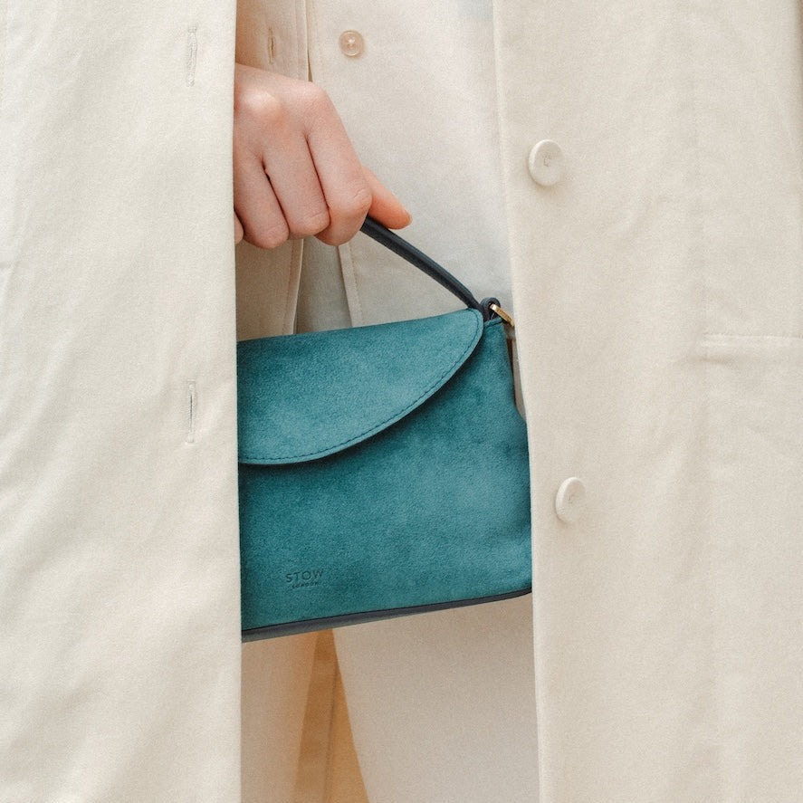 Model holding STOW London's Mini East West in Ocean Teal suede leather featuring gold-coated stainless steel hardware