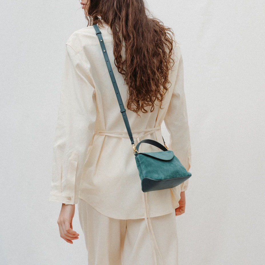 Model wearing STOW London's Mini East West in Ocean Teal suede leather crossbody featuring gold-coated stainless steel hardware