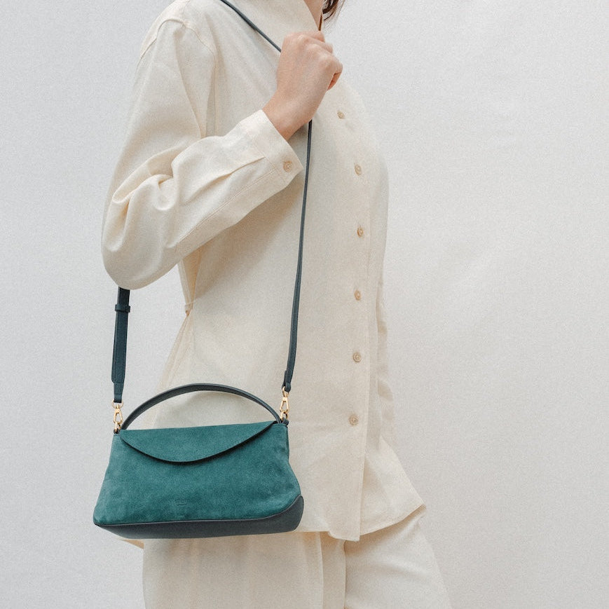 Model wearing STOW London's Mini East West in Ocean Teal suede leather on her shoulder featuring gold-coated stainless steel hardware