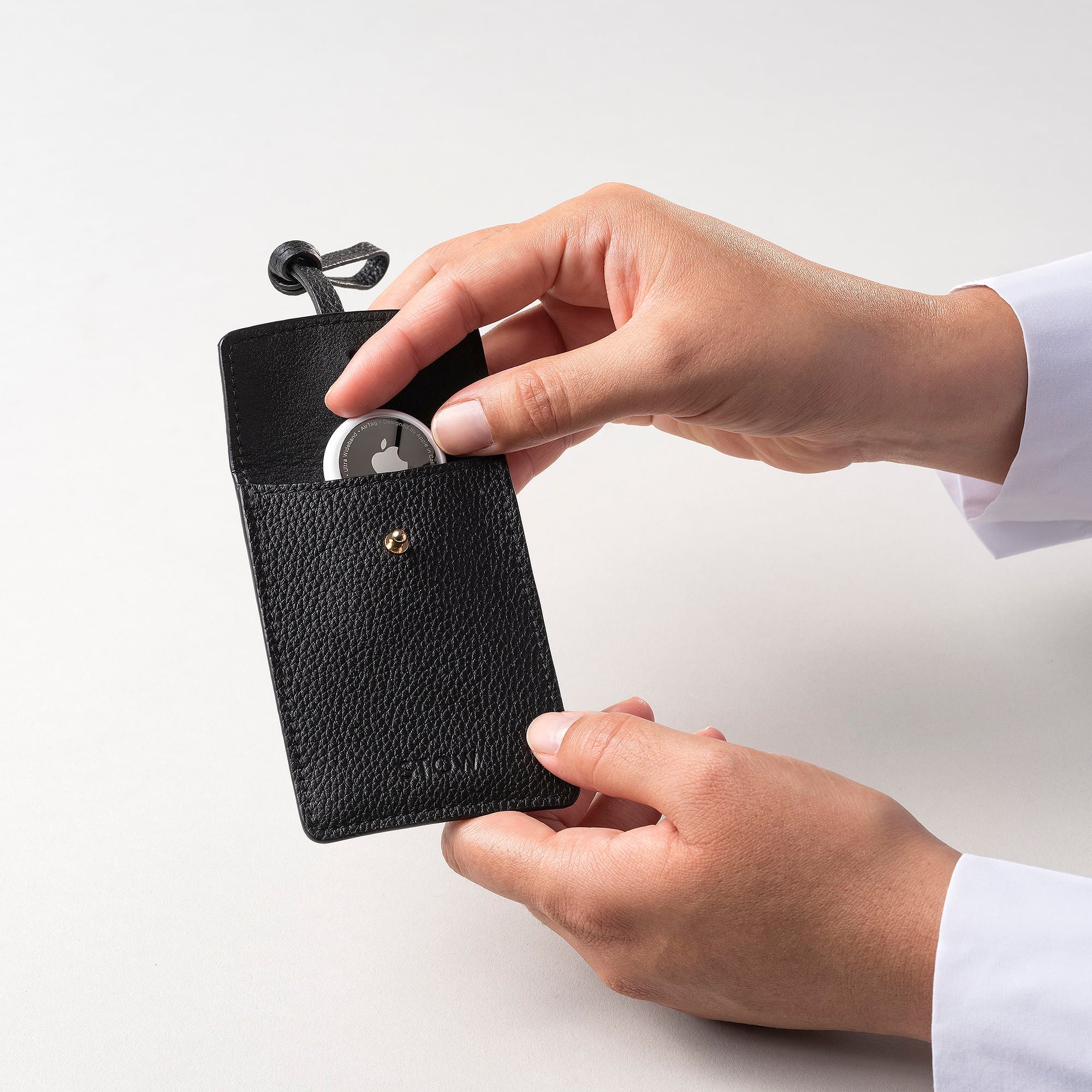 STOW London Leather Multi Tag in Black pebbled leather with model placing Apple AirTag inside.