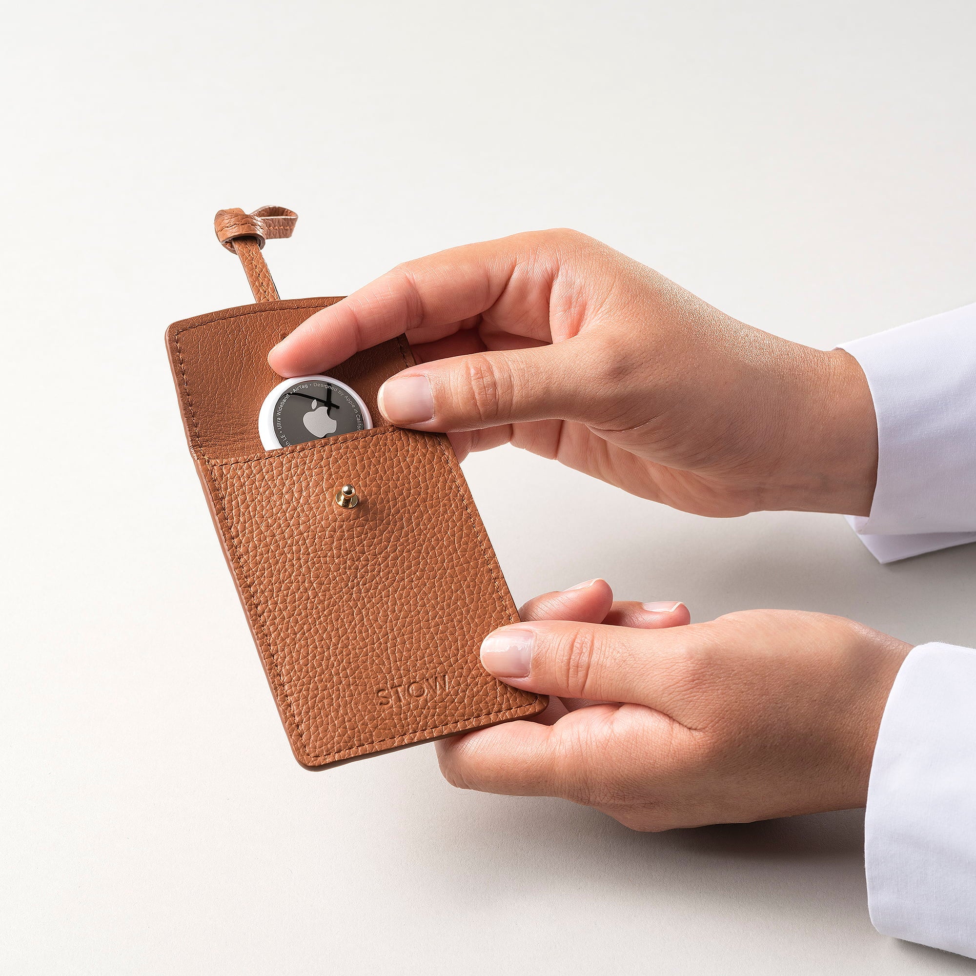 STOW London Leather Multi Tag in Earth Tan pebbled leather with model placing Apple AirTag inside.