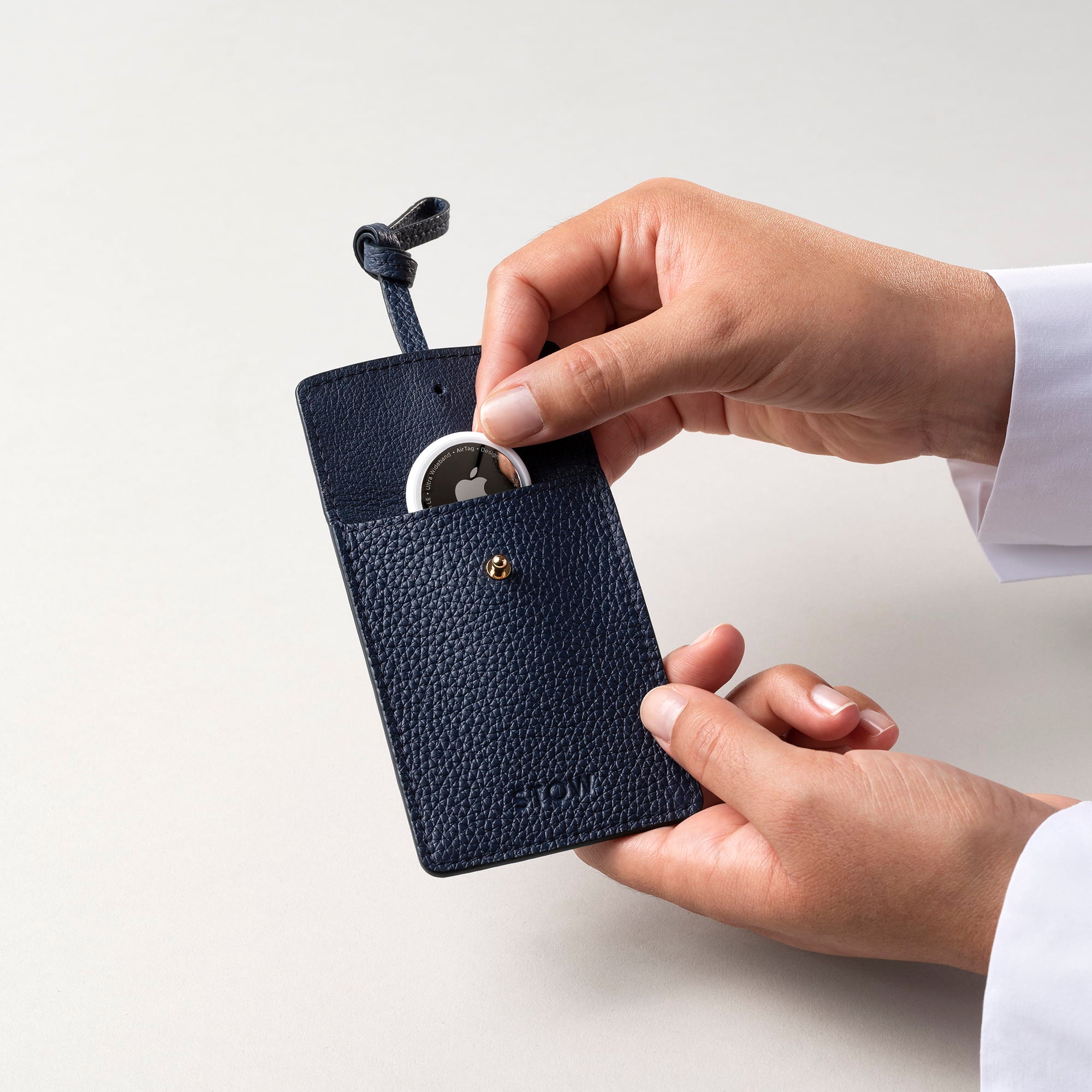 STOW London Leather Multi Tag in Navy pebbled leather with model placing Apple AirTag inside.