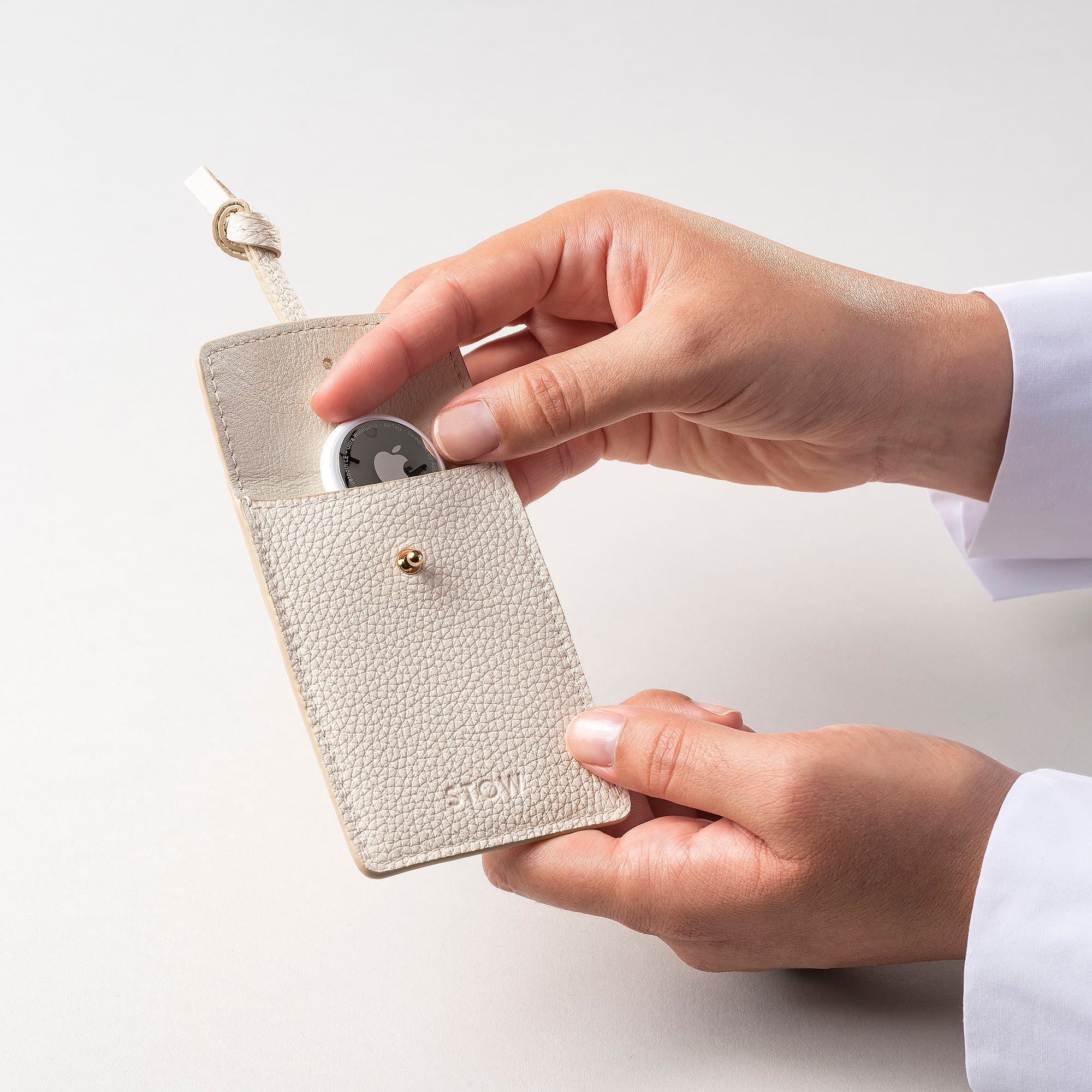 STOW London Leather Multi Tag in Spring Moon pebbled leather with model placing Apple AirTag inside.