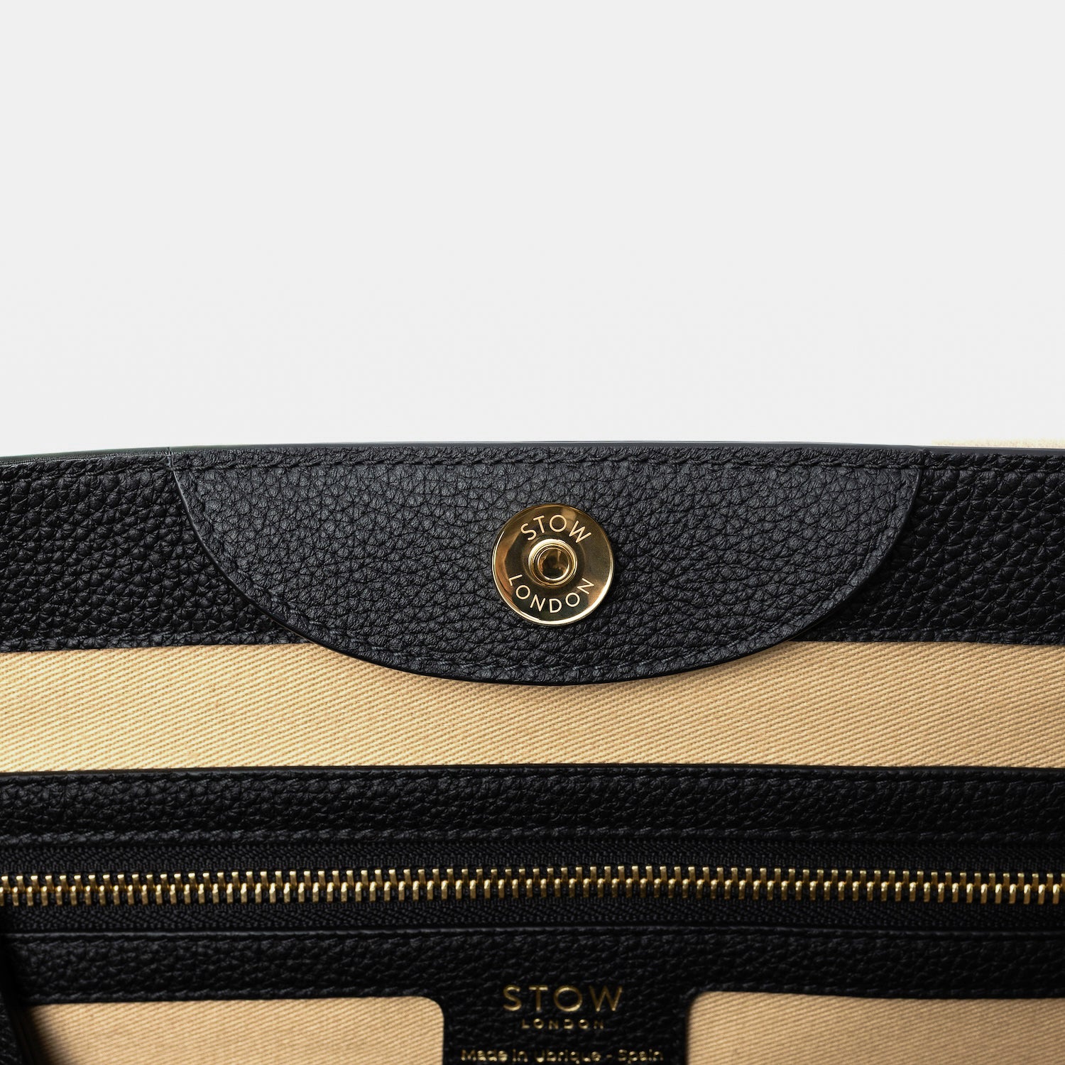 Close up of the magnet on STOW London's Nastro Tote bag in Black pebbled leather featuring a zip pocket on a light grey background