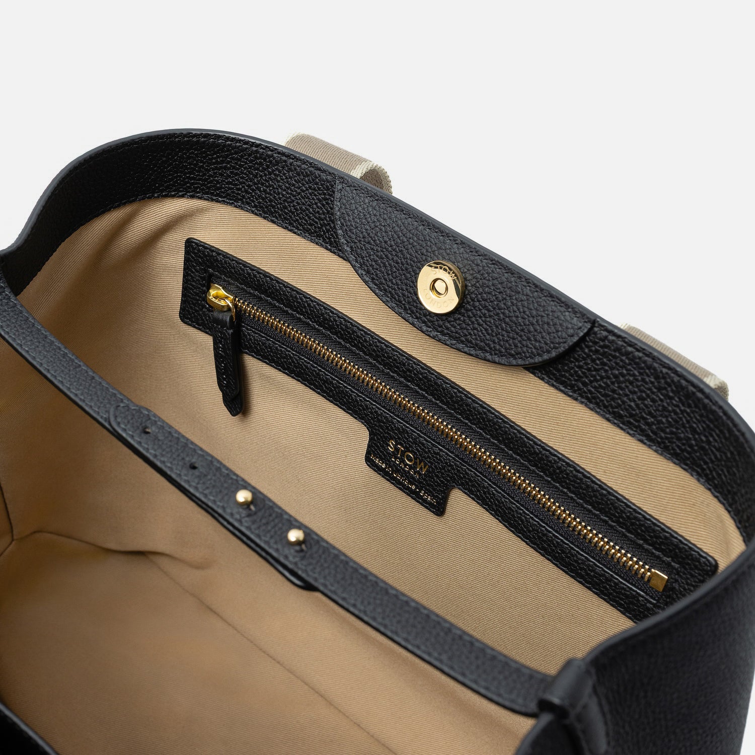 Close up of the cotton interior of STOW London's Nastro Tote bag in Black pebbled leather featuring a zip pocket and leather strap on a light grey background