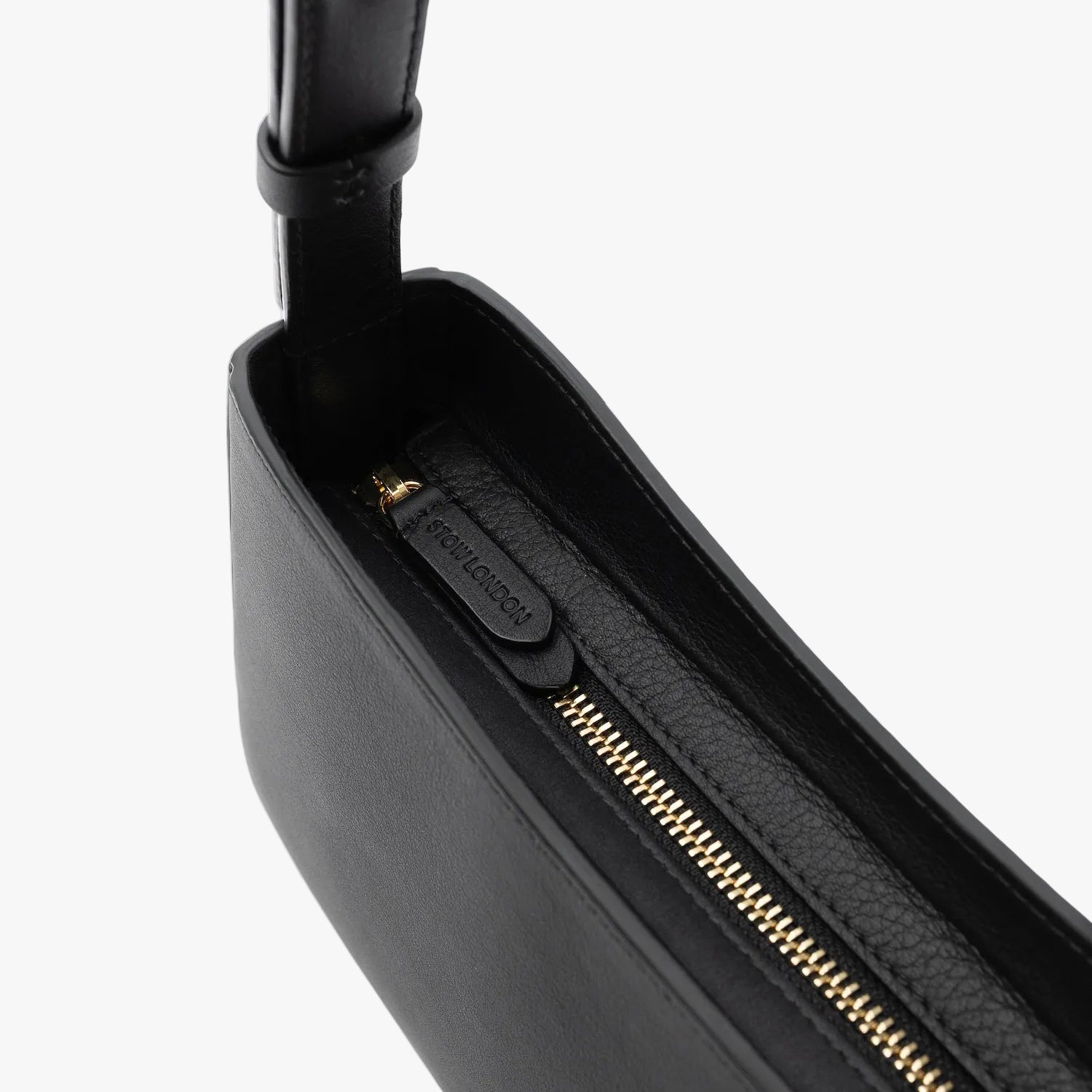 Close up of the gold zip closure and STOW London embossed pull tabs on Stow London's Post Shoulder in Black smooth leather on a light grey background