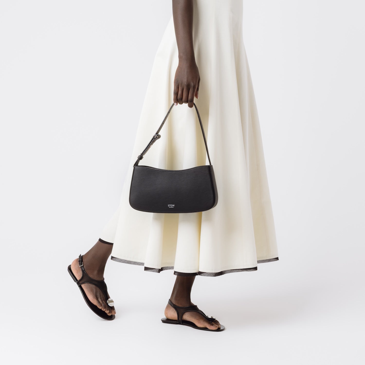 Model carrying STOW London's Post Shoulder bag in Black smooth leather at her side featuring silver hardware on a white background